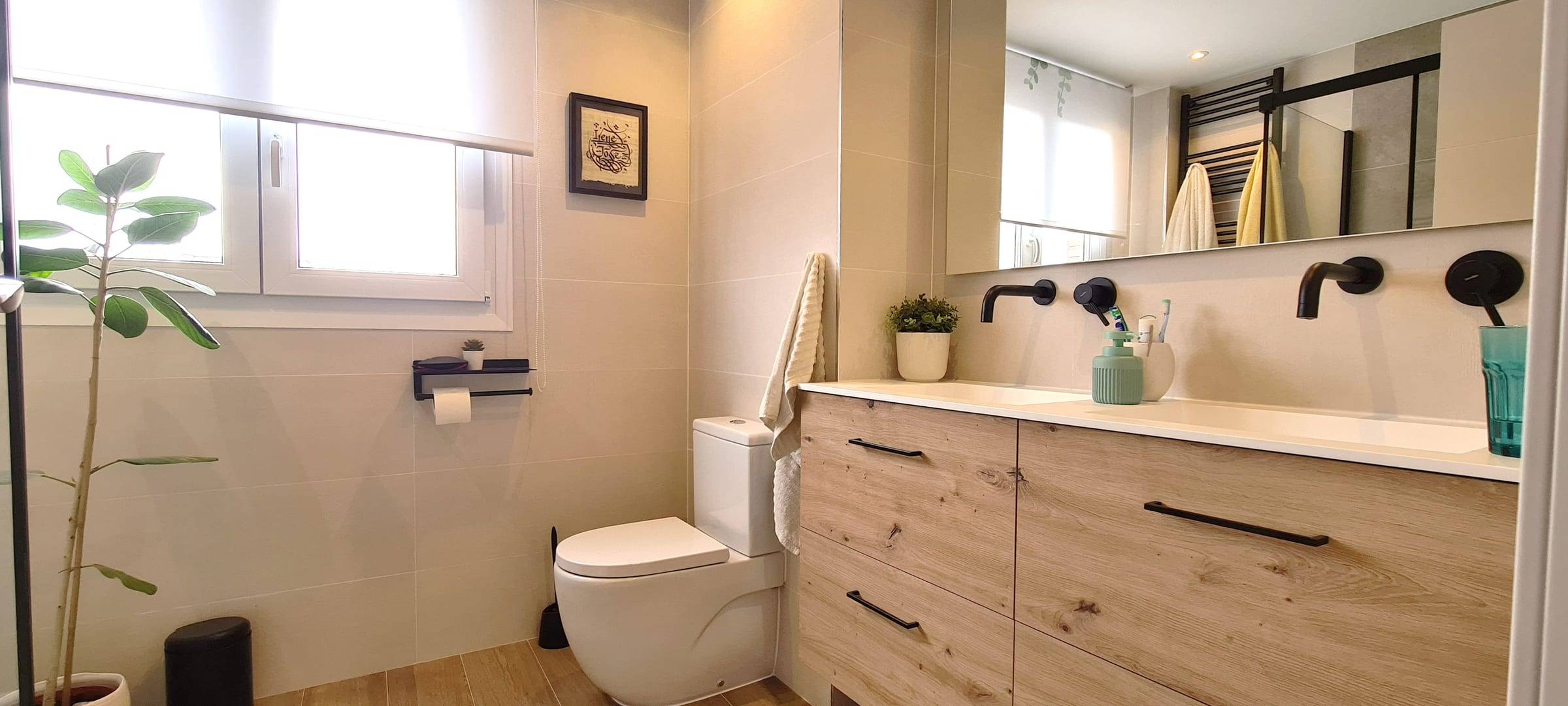 Baño reformado con mueble de lavabo de madera, grifería negra y ventana