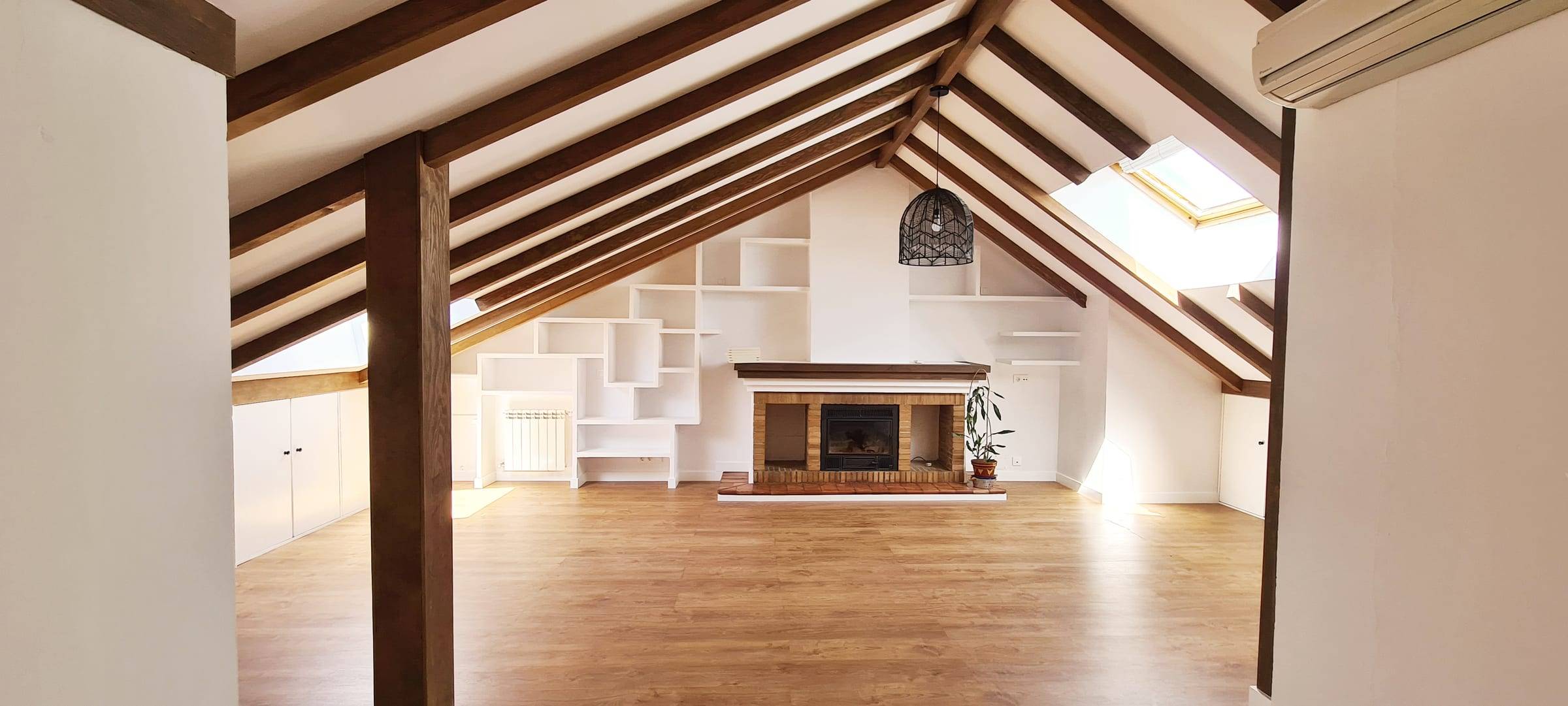 Buhardilla diáfana con vigas de madera, ventanas de tejado y estantería de obra