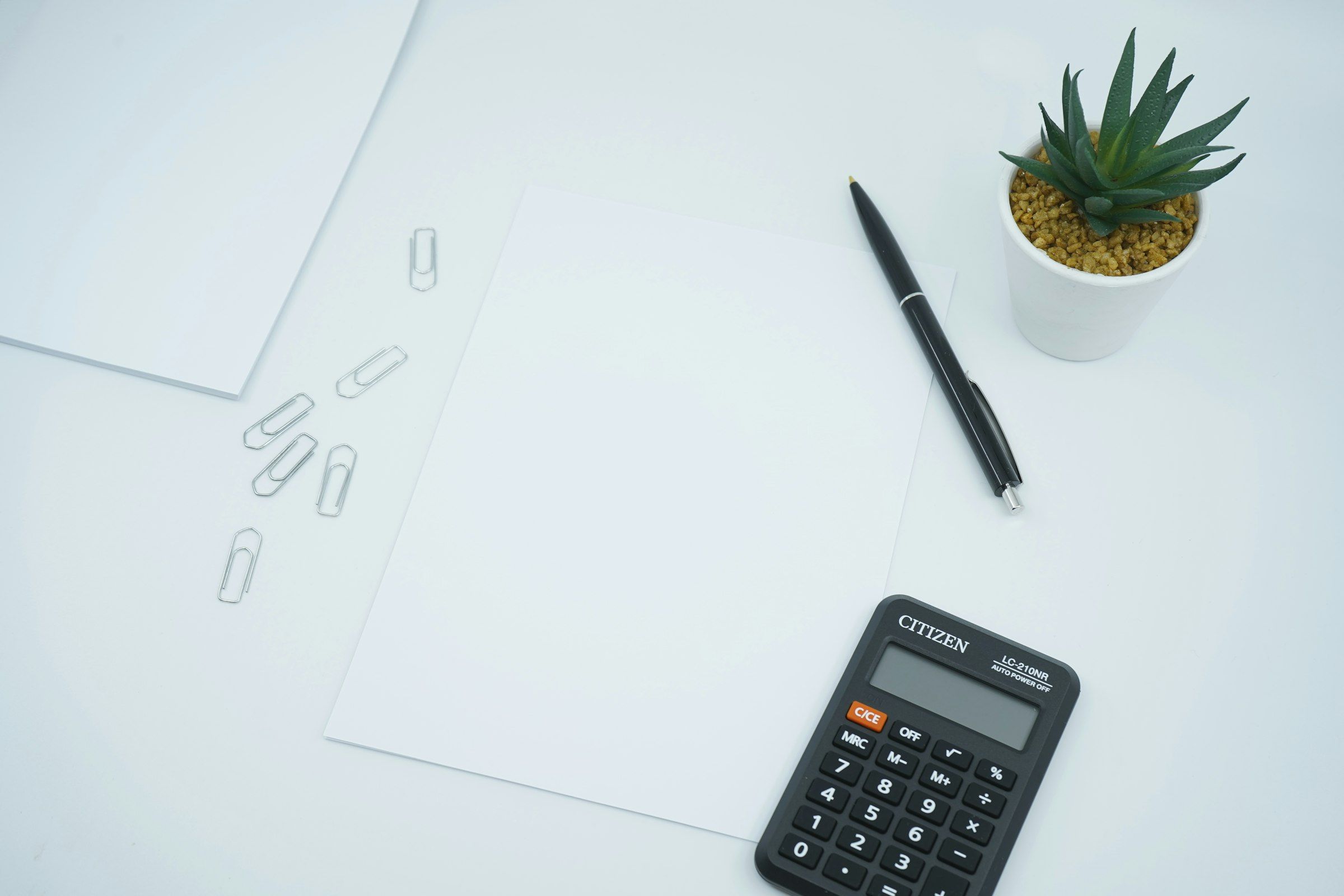 Calculadora, bolígrafo y hojas en blanco sobre una mesa clara