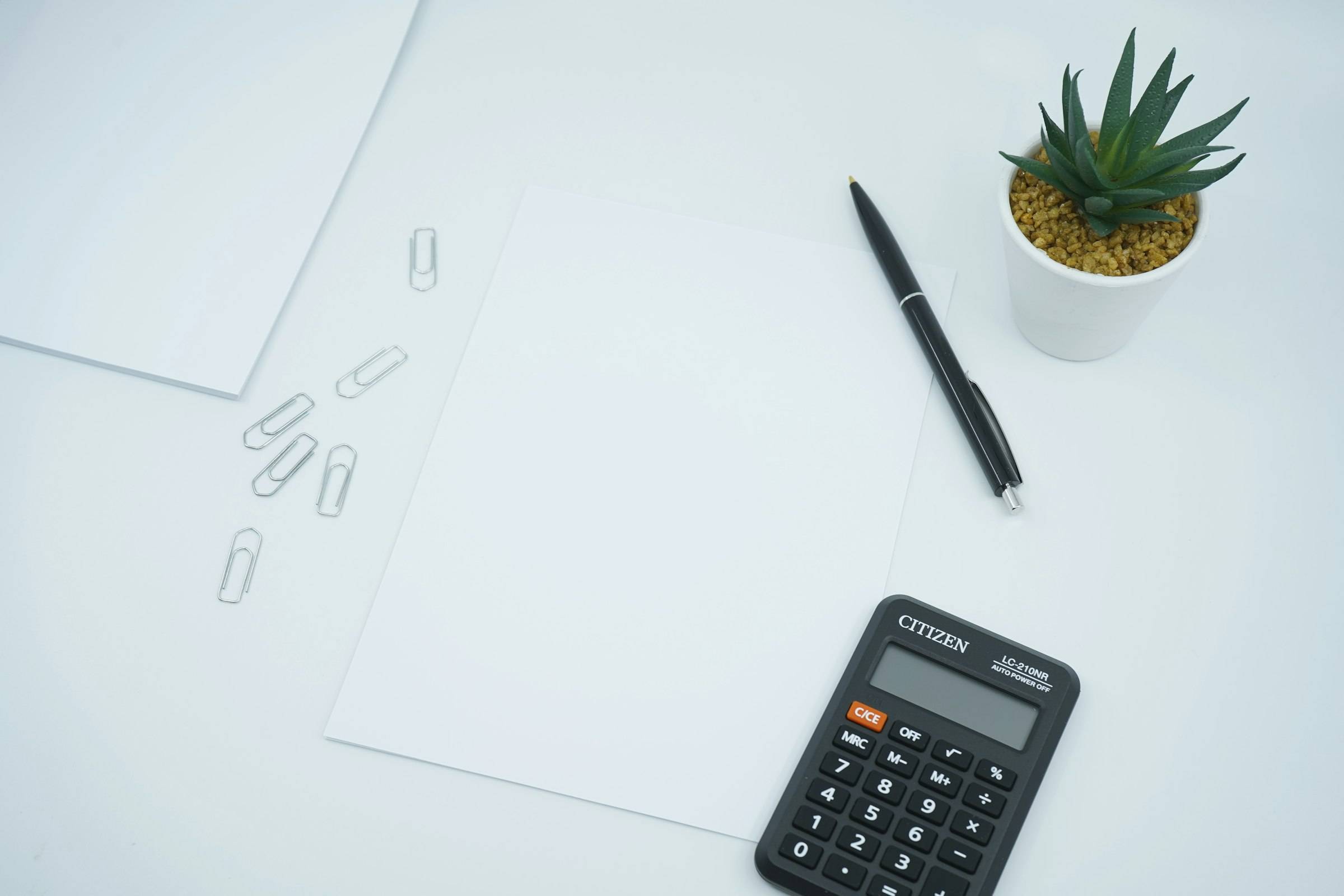 Calculadora, bolígrafo y hojas en blanco sobre una mesa clara