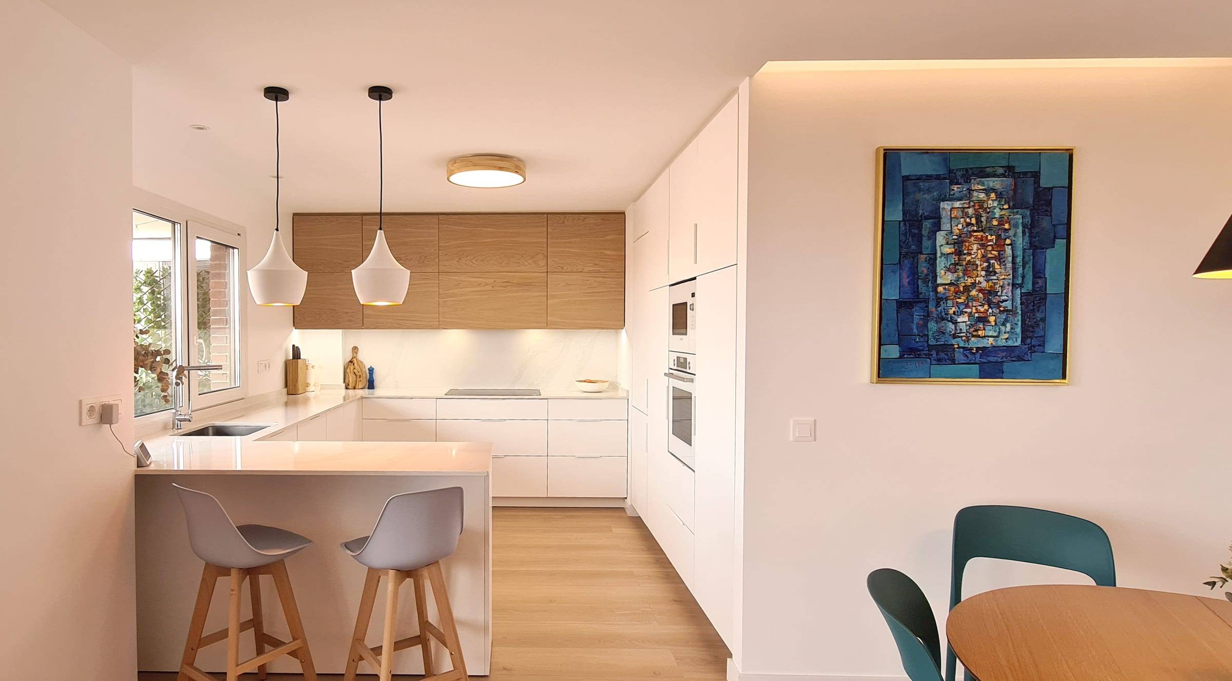 Cocina abierta al comedor con barra de desayuno, taburetes y muebles blancos y de madera