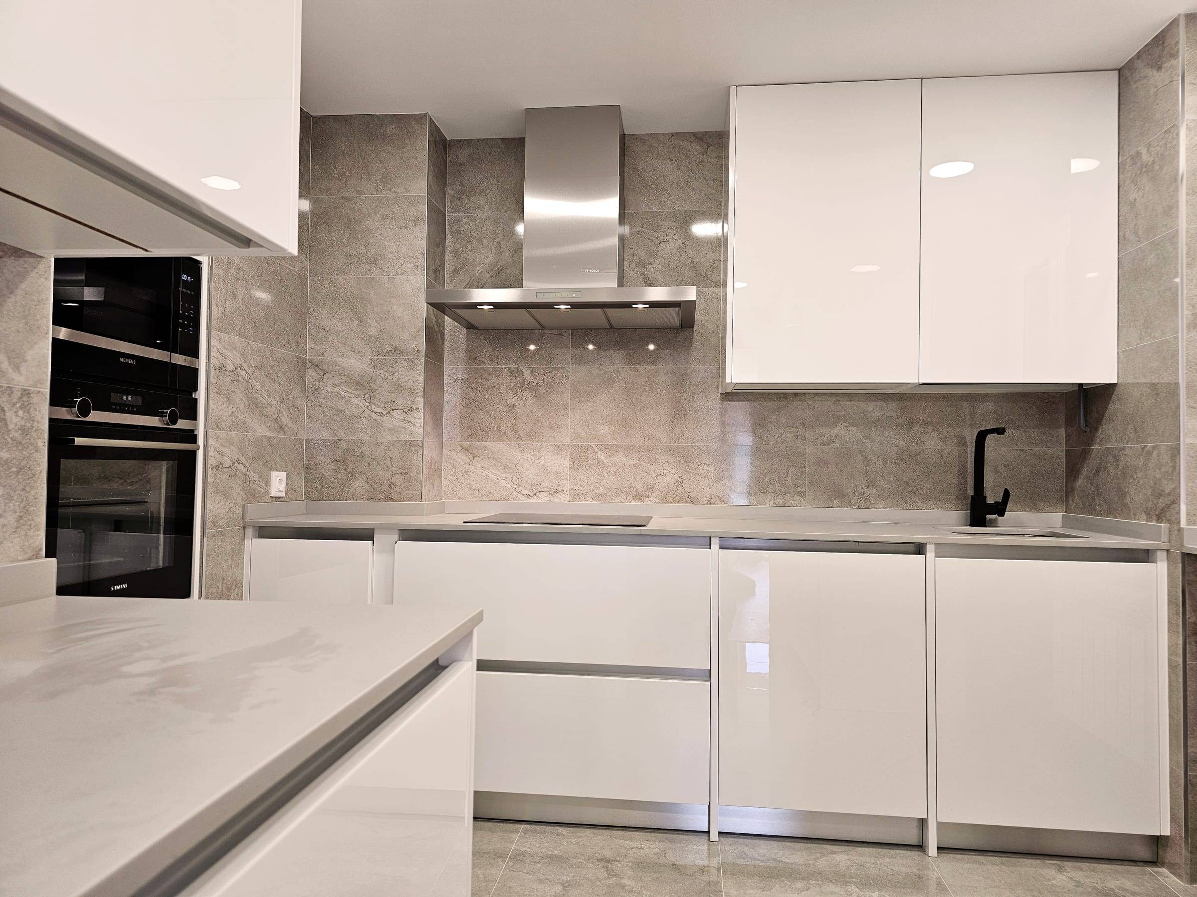 Cocina reformada con muebles blancos de brillo, encimera gris y horno en columna