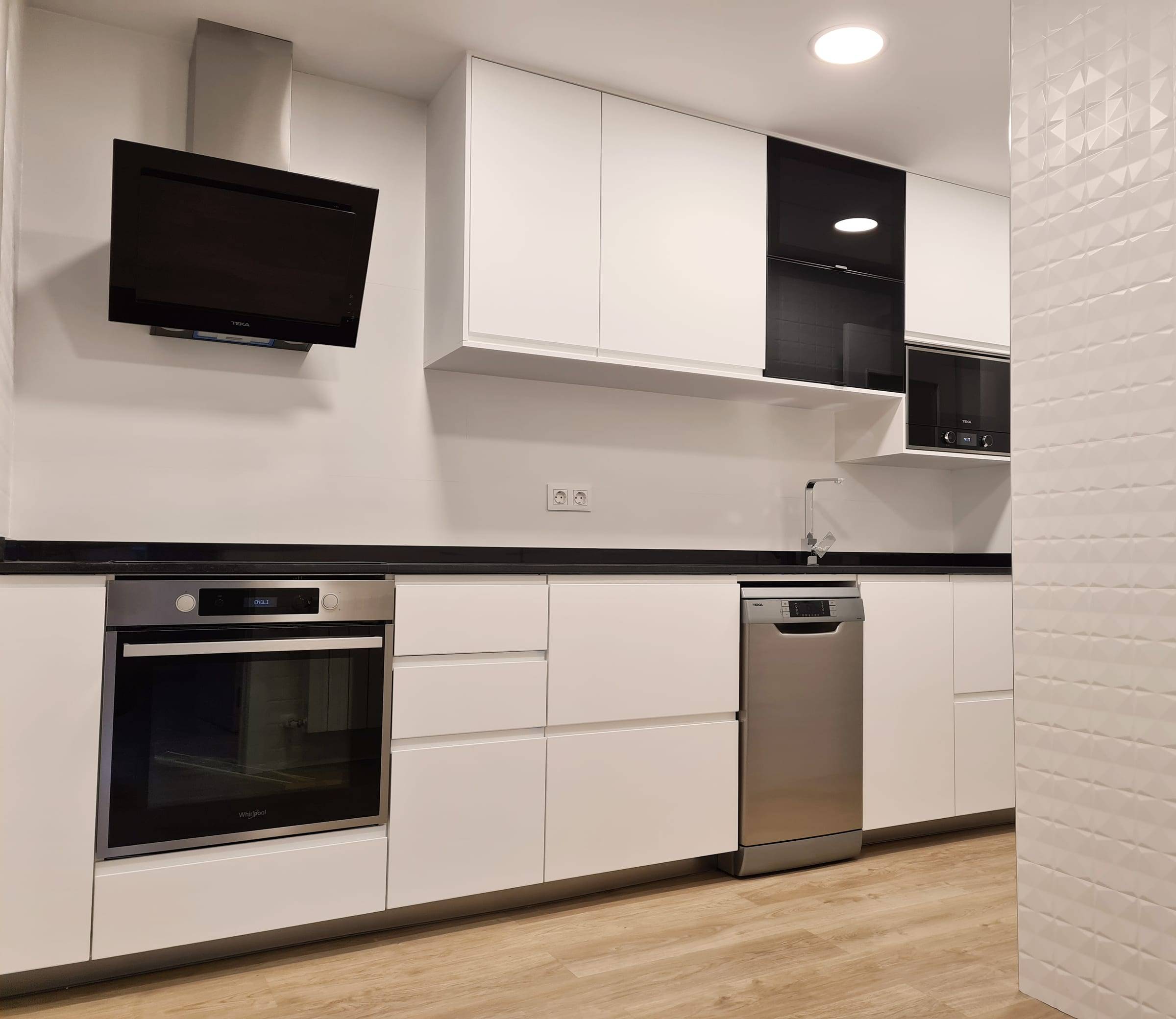 Cocina reformada con muebles blancos, encimera negra y azulejo blanco biselado