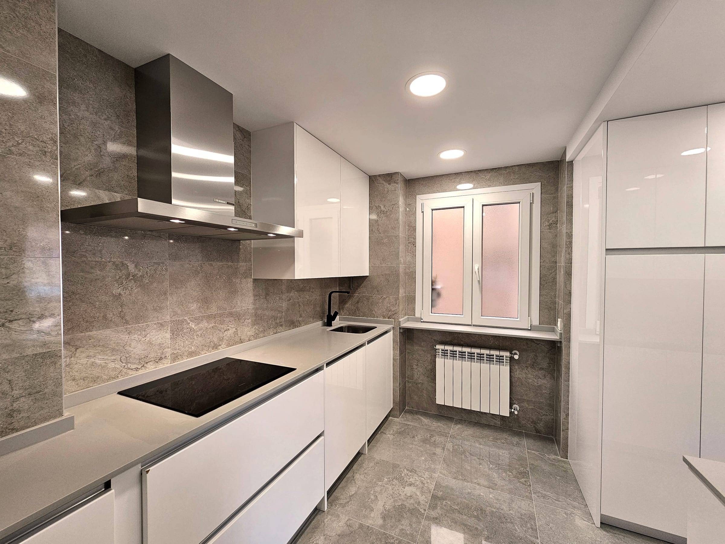 Cocina reformada con muebles blancos, encimera y revestimiento gris y campana de acero