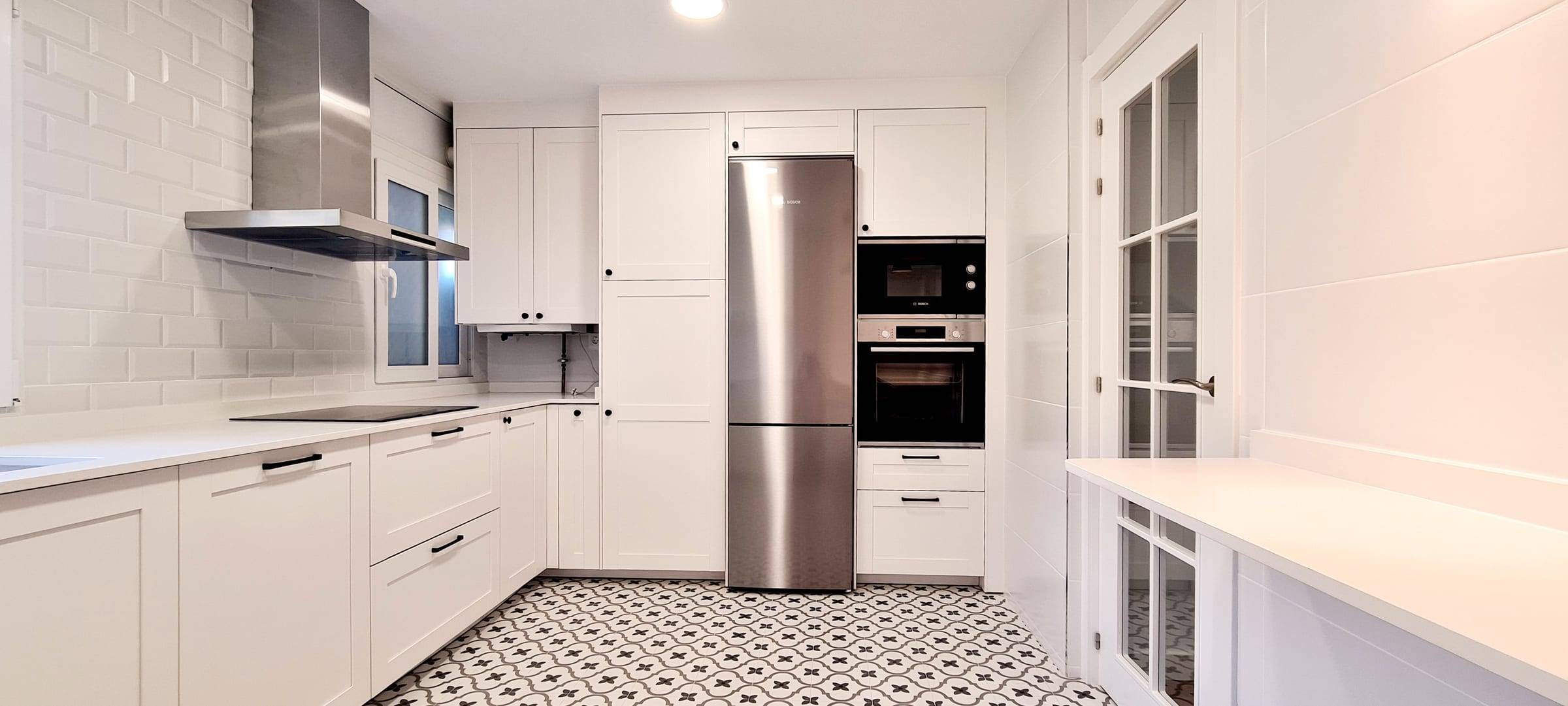 Cocina reformada con muebles blancos de cuarterones y suelo hidráulico