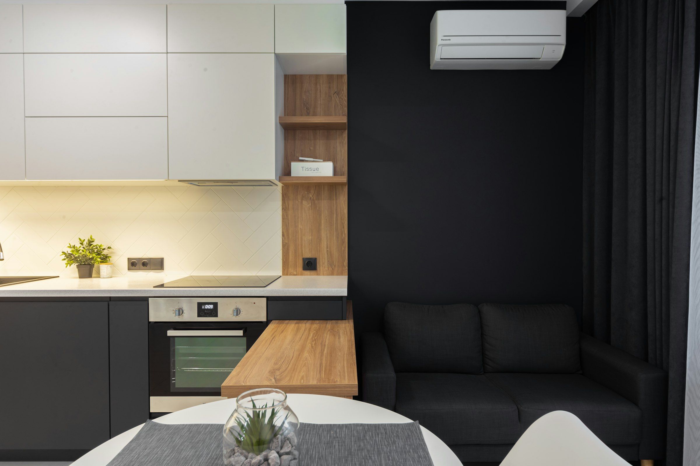 Cocina abierta al salón con un split de aire acondicionado sobre la pared oscura