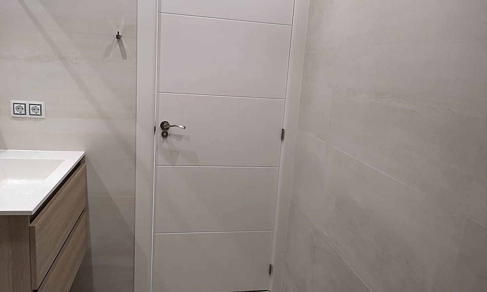 Puerta lacada en blanco del baño, con alicatado claro de gran formato
