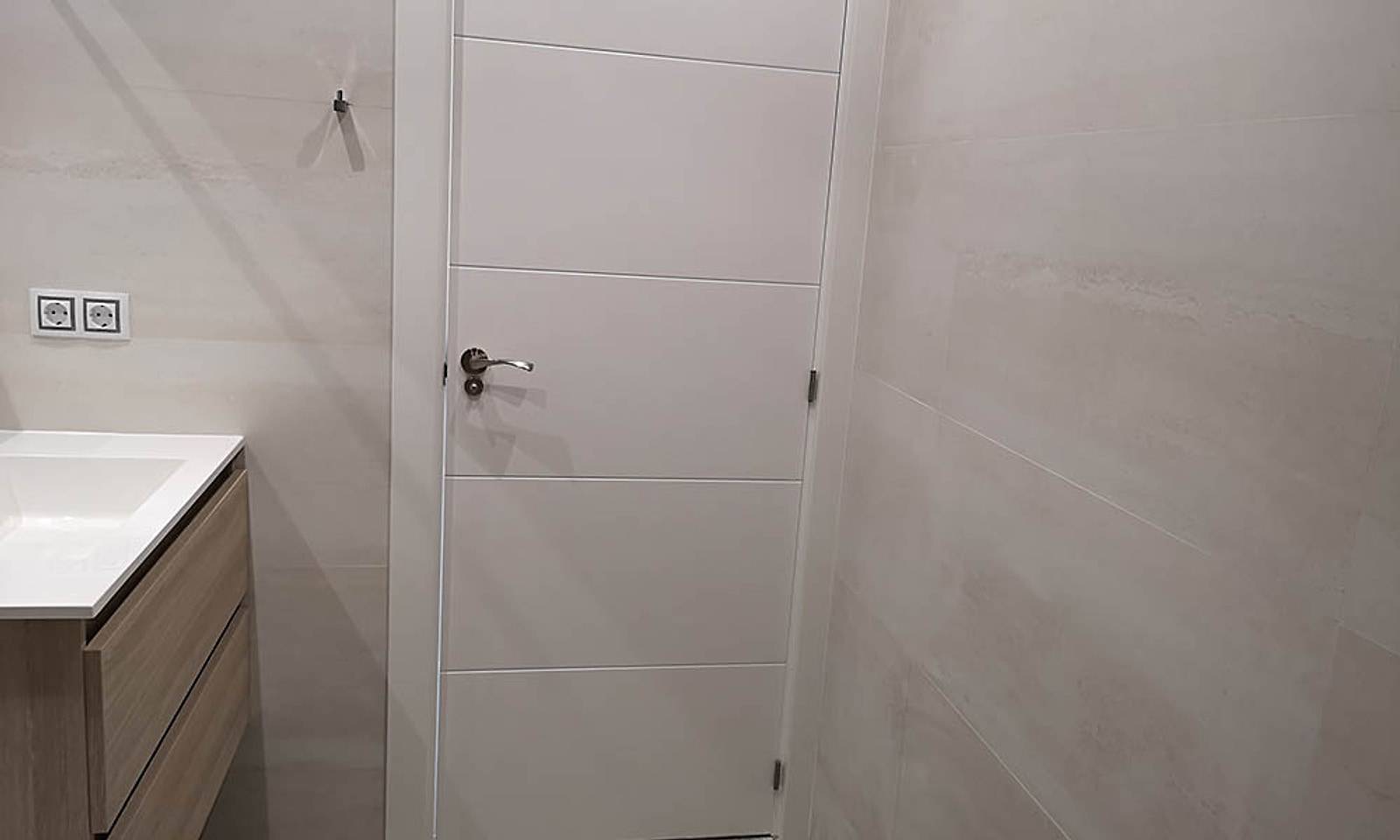 Puerta lacada en blanco del baño, con alicatado claro de gran formato