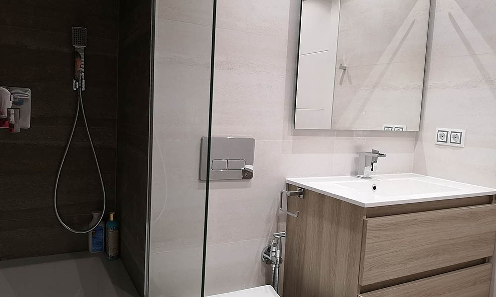 Lavabo con mueble color madera, espejo y el grifo mezclador junto al inodoro