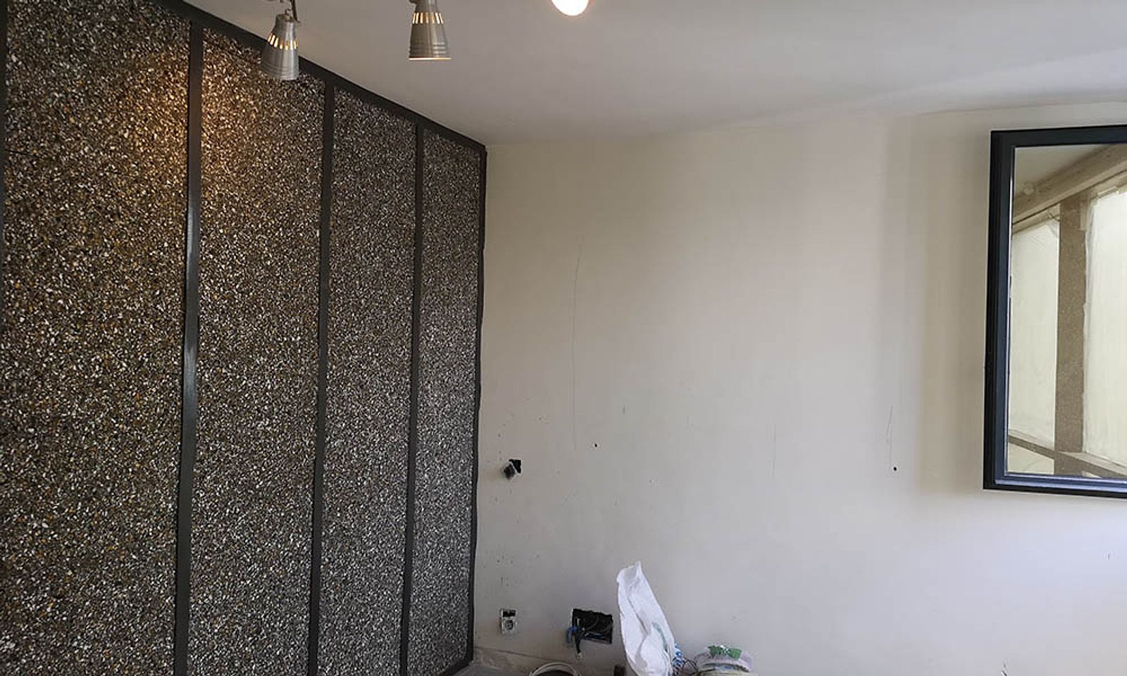 Vivienda antes de la reforma, con una pared de revestimiento antiguo y focos de carril