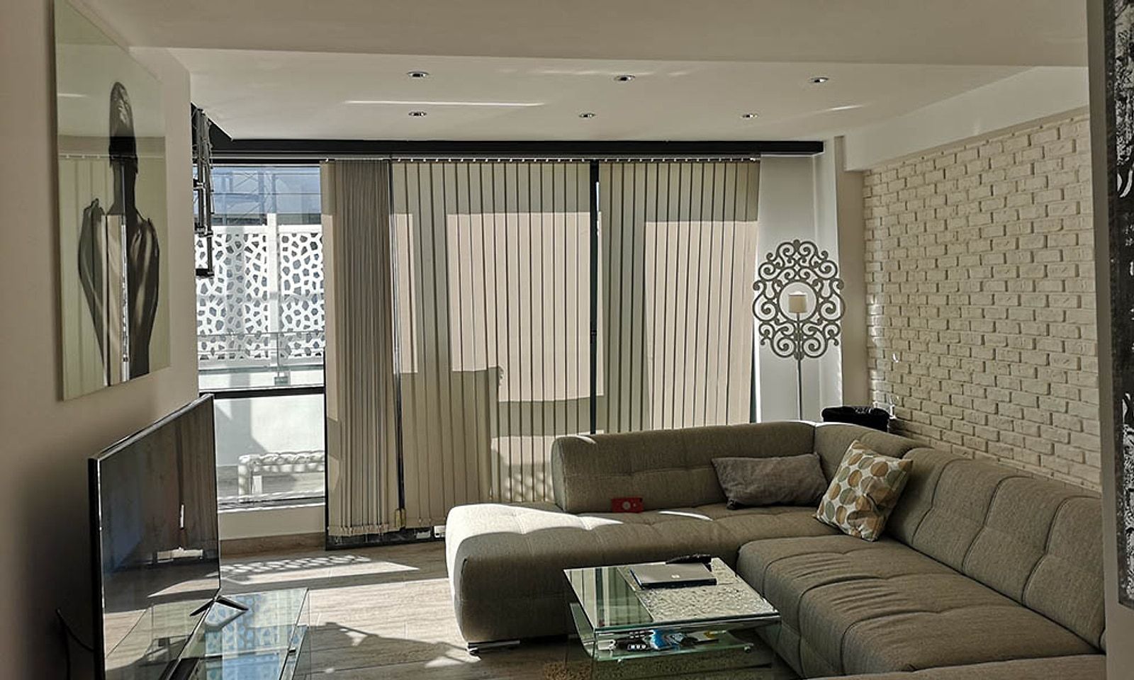 Planta baja del loft terminada, con sofá rinconera, pared de ladrillo blanco y cortinas