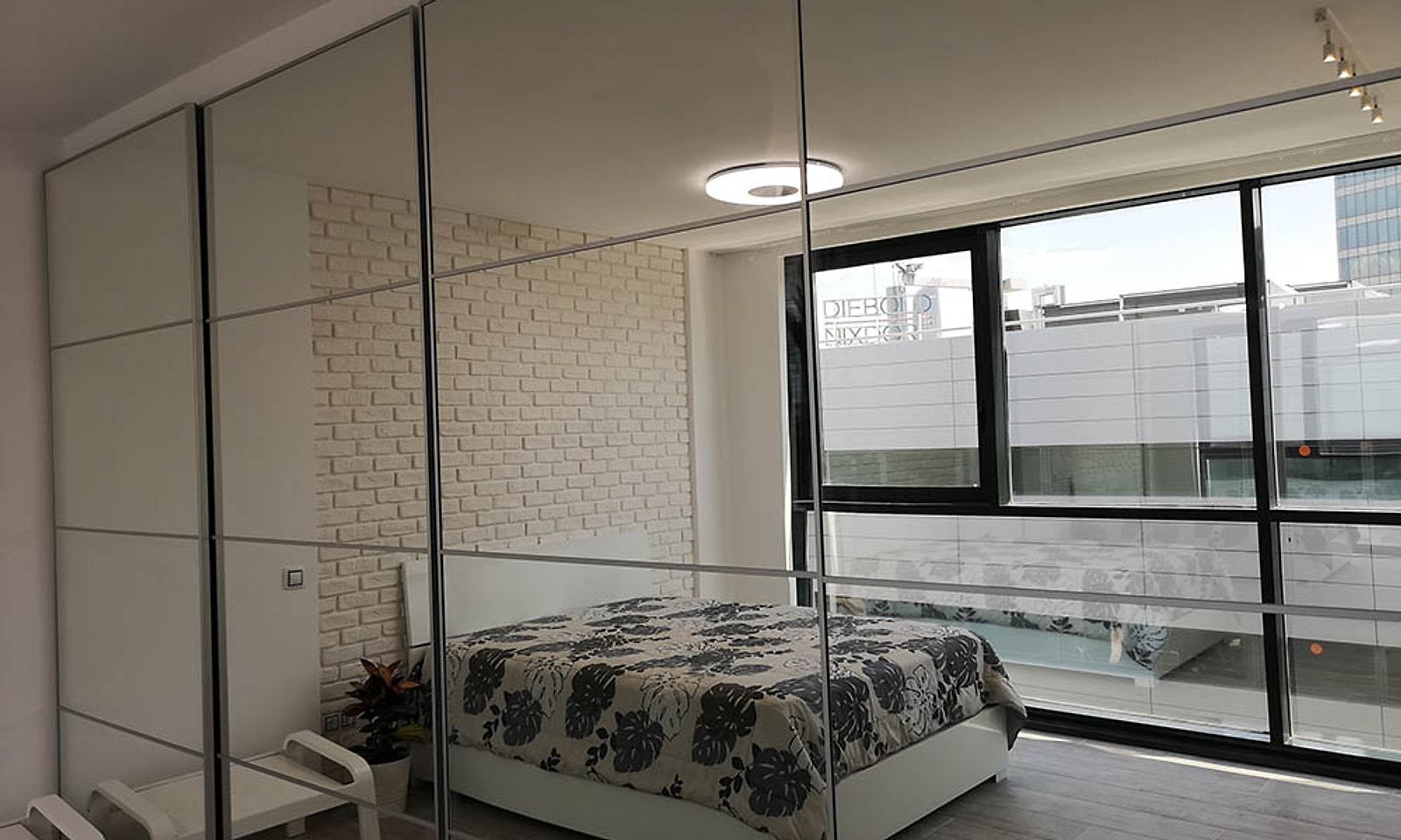 La misma planta convertida en dormitorio, con armario de espejo y cama junto al ventanal