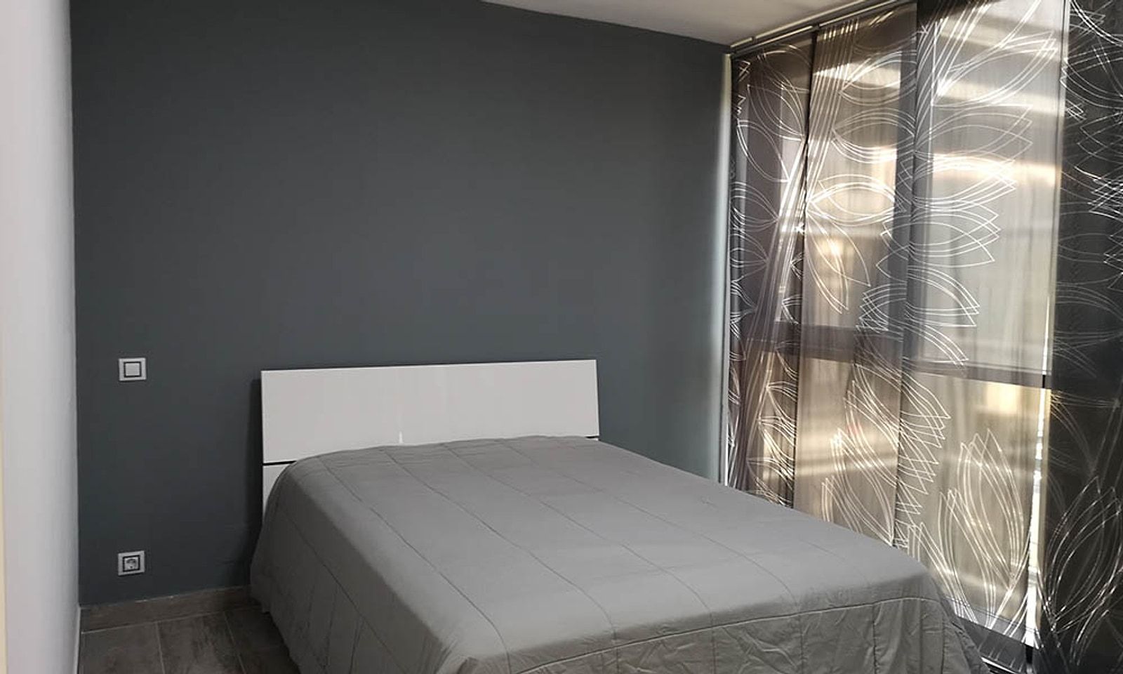 La misma habitación terminada, con la pared gris y una cama de matrimonio