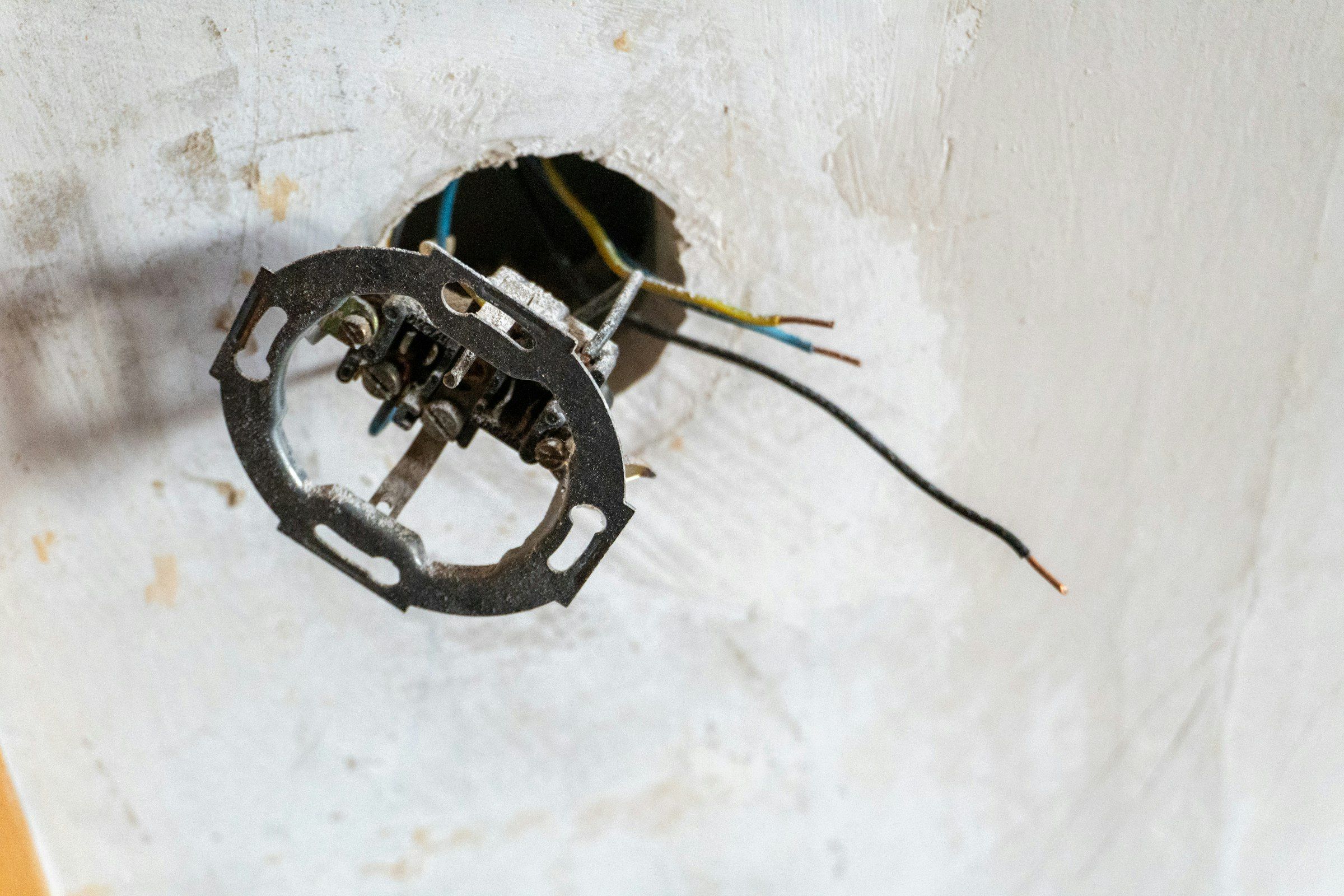 Mecanismo de enchufe antiguo desmontado, con los cables a la vista en una pared en obra