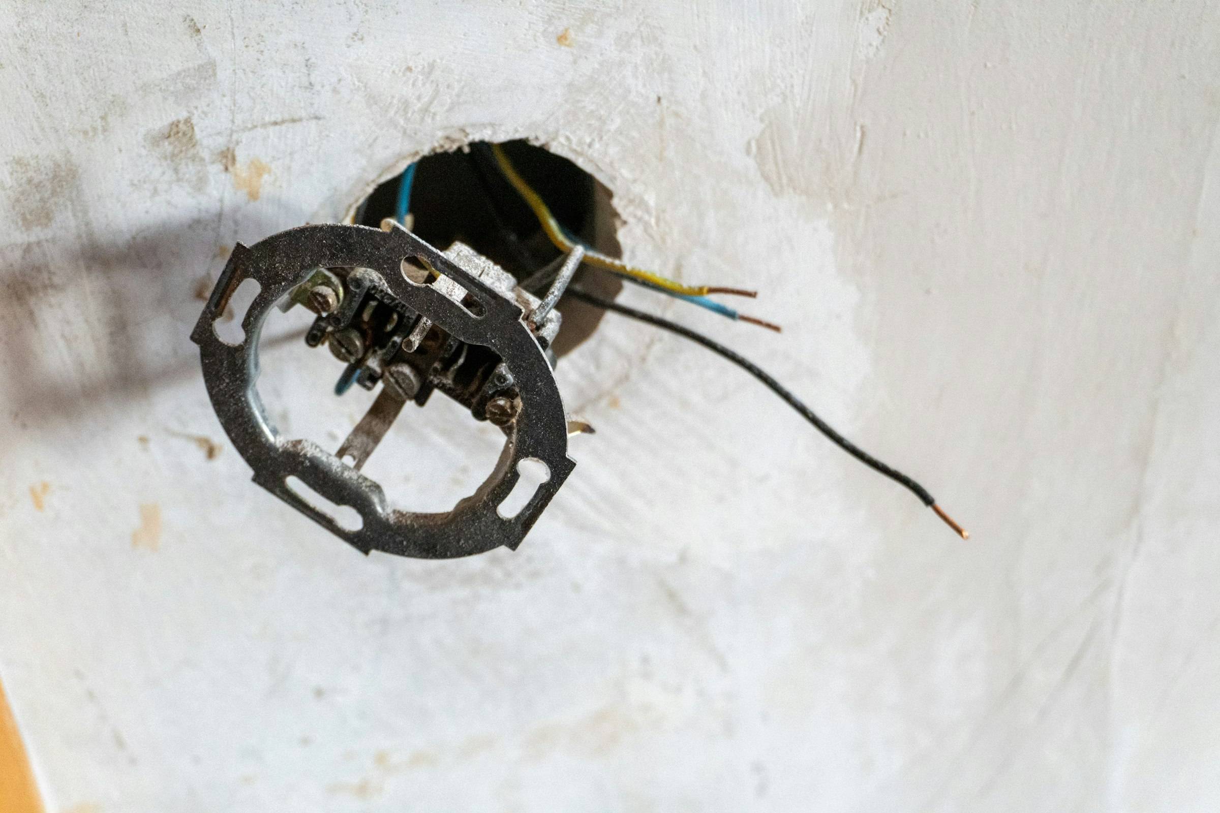 Mecanismo de enchufe antiguo desmontado, con los cables a la vista en una pared en obra