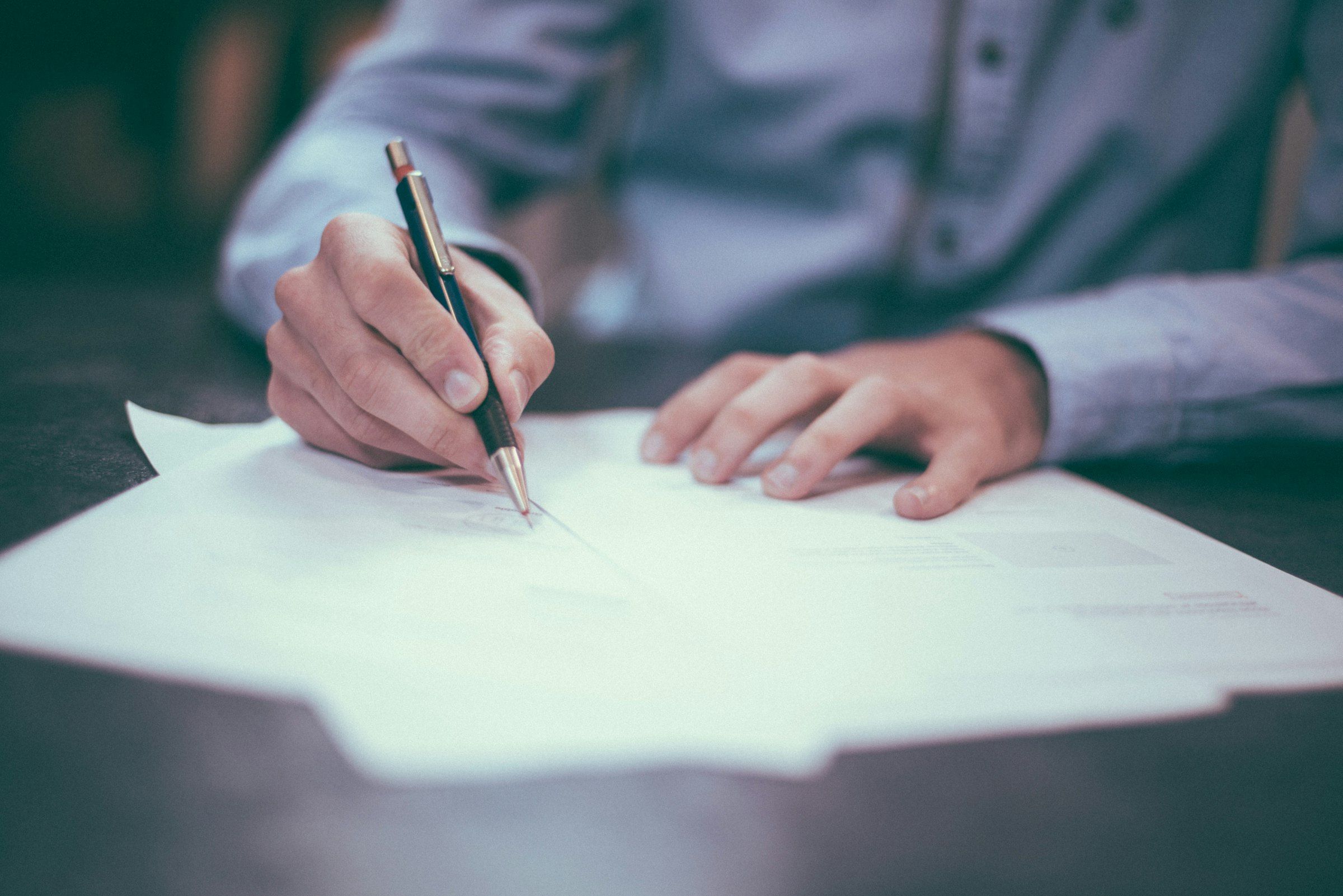 Mano que firma un documento sobre una mesa