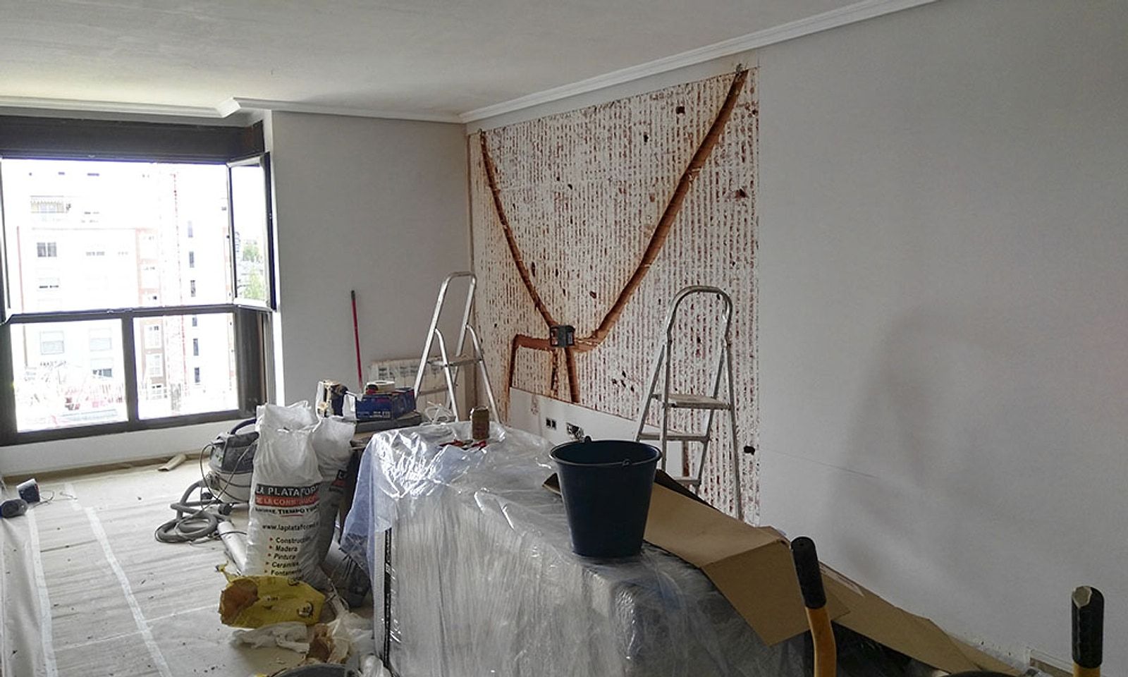 Salón del piso durante la obra, con el suelo protegido y material de pintura