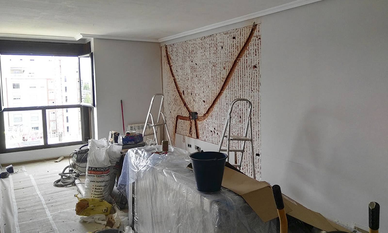 Salón del piso durante la obra, con el suelo protegido y material de pintura