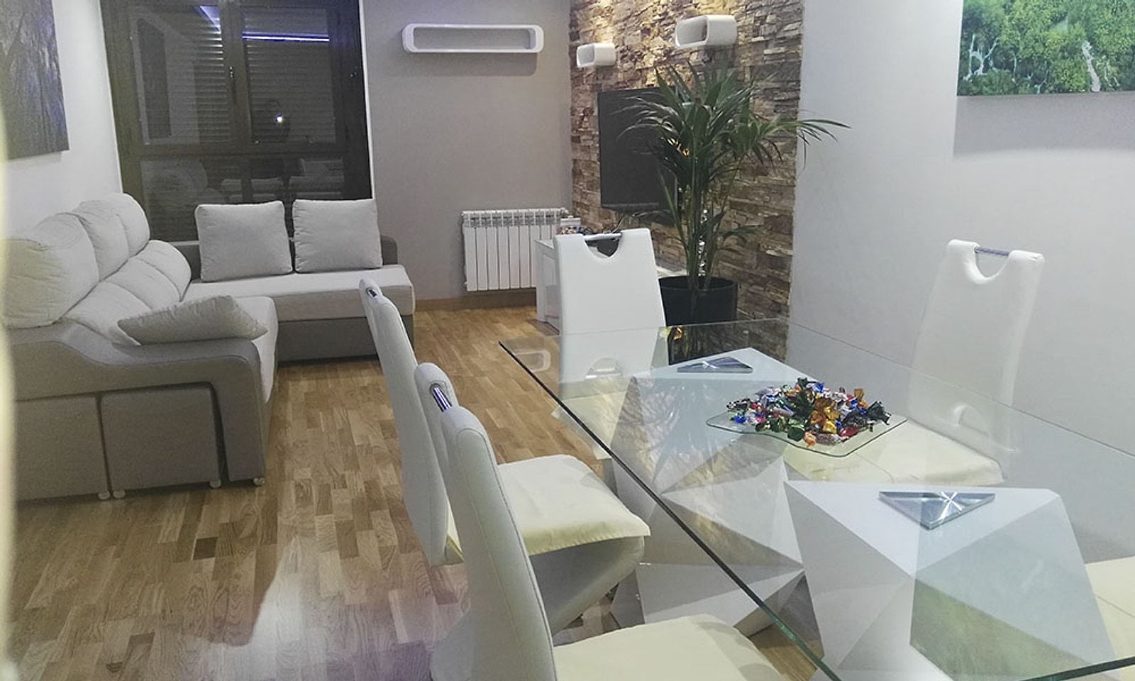 Salón comedor con sofá, mesa de cristal y sillas blancas