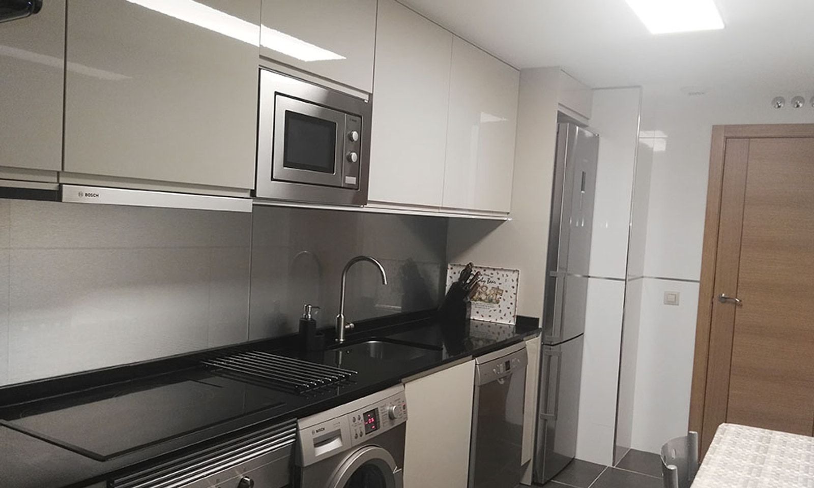Cocina con muebles blancos, microondas en alto y panel de aluminio en la pared
