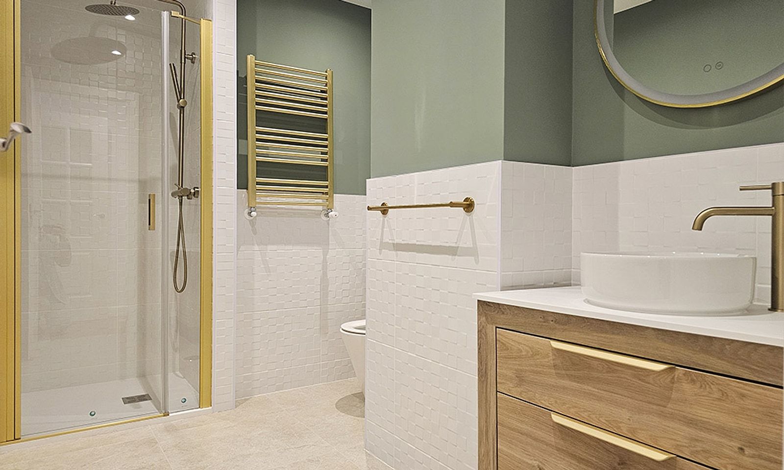 Baño con ducha de mampara dorada, pared verde, lavabo sobre encimera de madera y grifería dorada