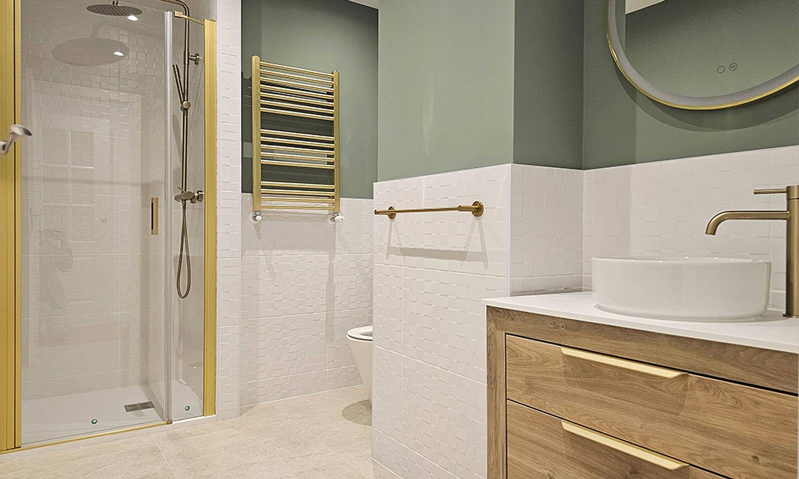 Baño con ducha de mampara dorada, pared verde, lavabo sobre encimera de madera y grifería dorada