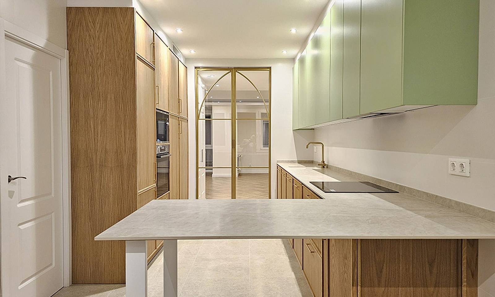 Cocina del piso con muebles de madera, armarios altos verdes, península y el cerramiento de cristal y hierro dorado al fondo