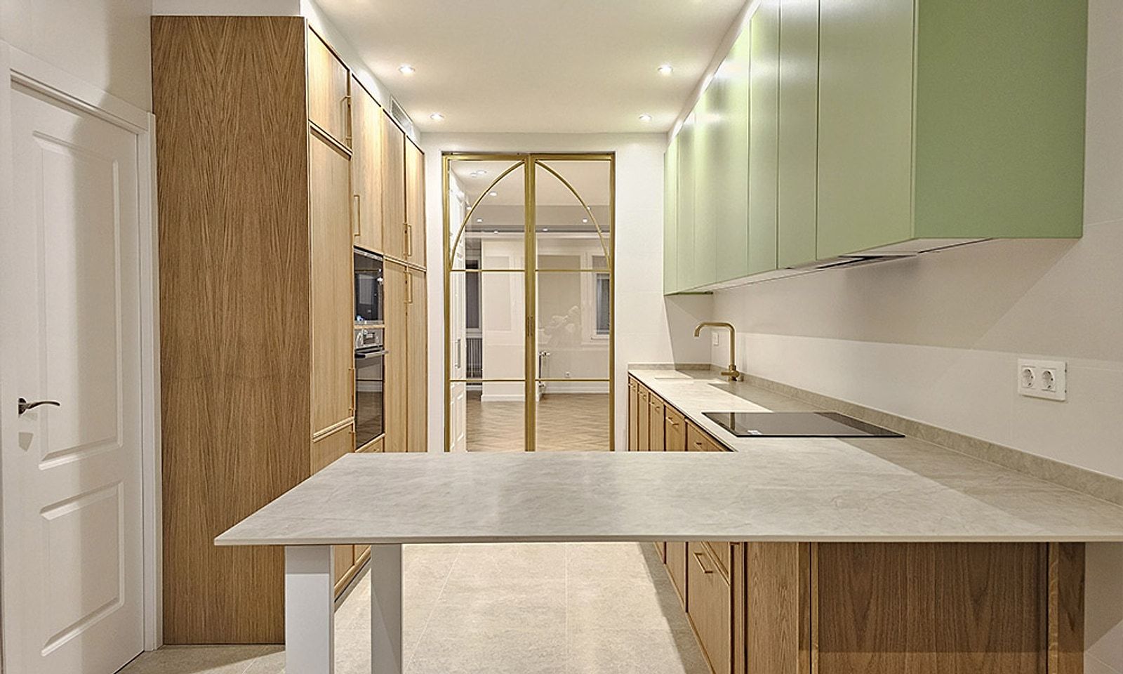 Cocina del piso con muebles de madera, armarios altos verdes, península y el cerramiento de cristal y hierro dorado al fondo