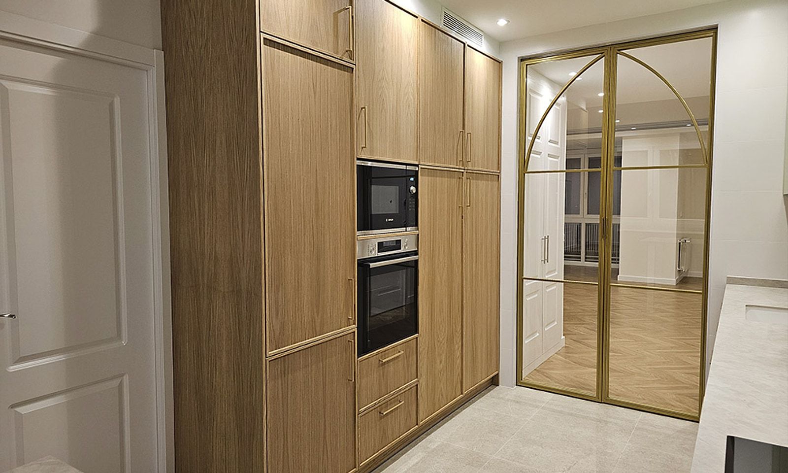 Columna de madera con horno y microondas junto a la corredera de cristal y hierro dorado