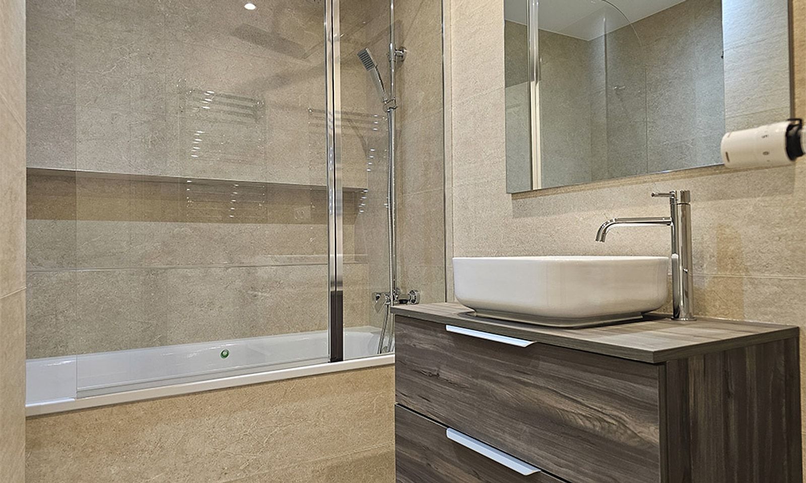 Baño con bañera y mampara, lavabo sobre mueble de madera y espejo