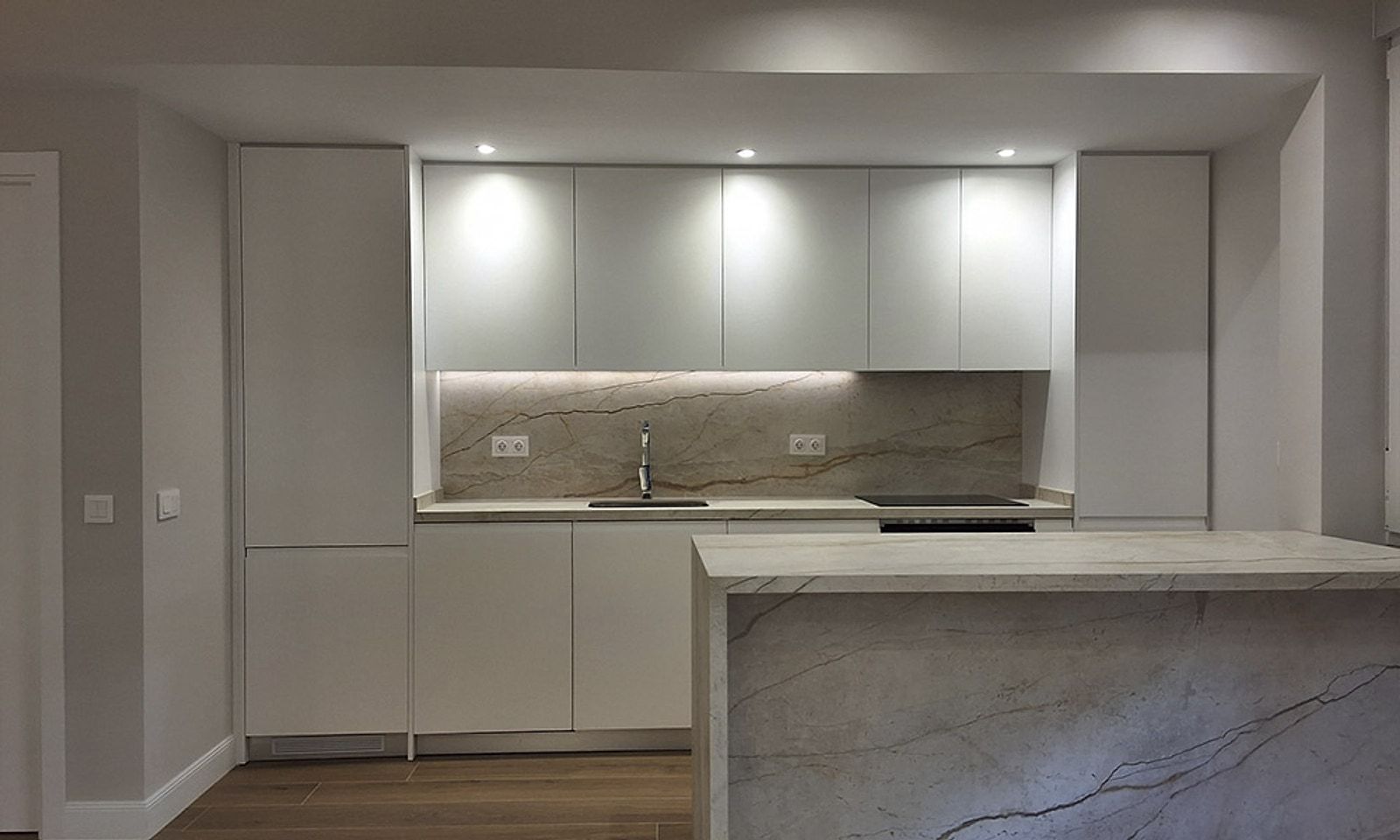 Cocina blanca con luz bajo los muebles altos e isla de mármol con vetas grises