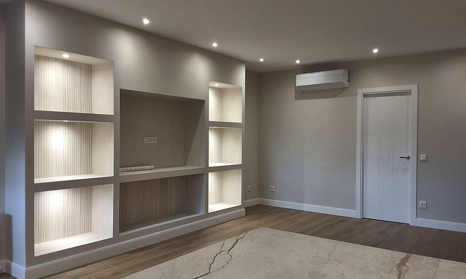 Salón reformado con estantería empotrada iluminada y suelo de madera