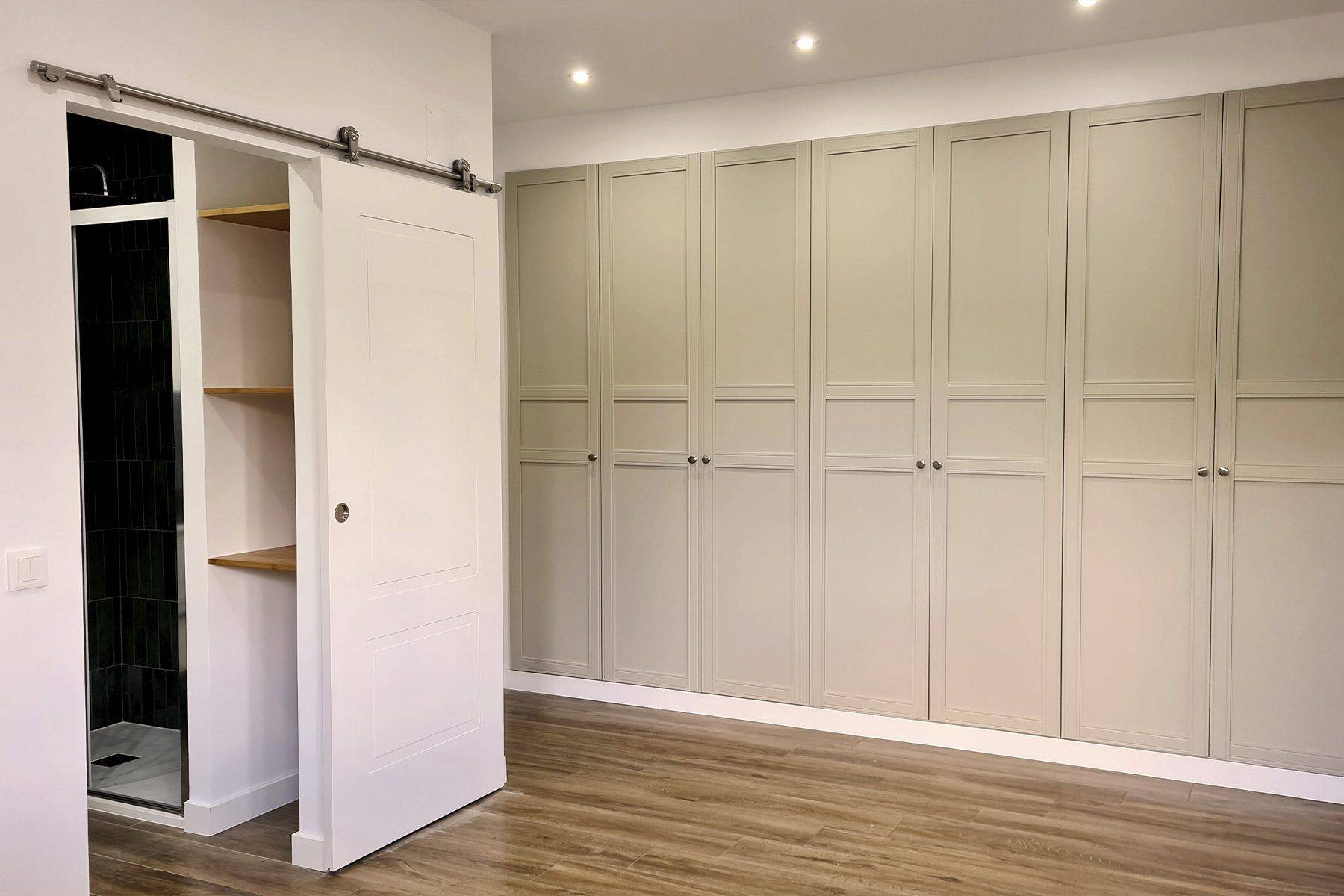 Dormitorio con armario empotrado de puertas de cuarterones en beige y una puerta corredera de granero hacia el baño