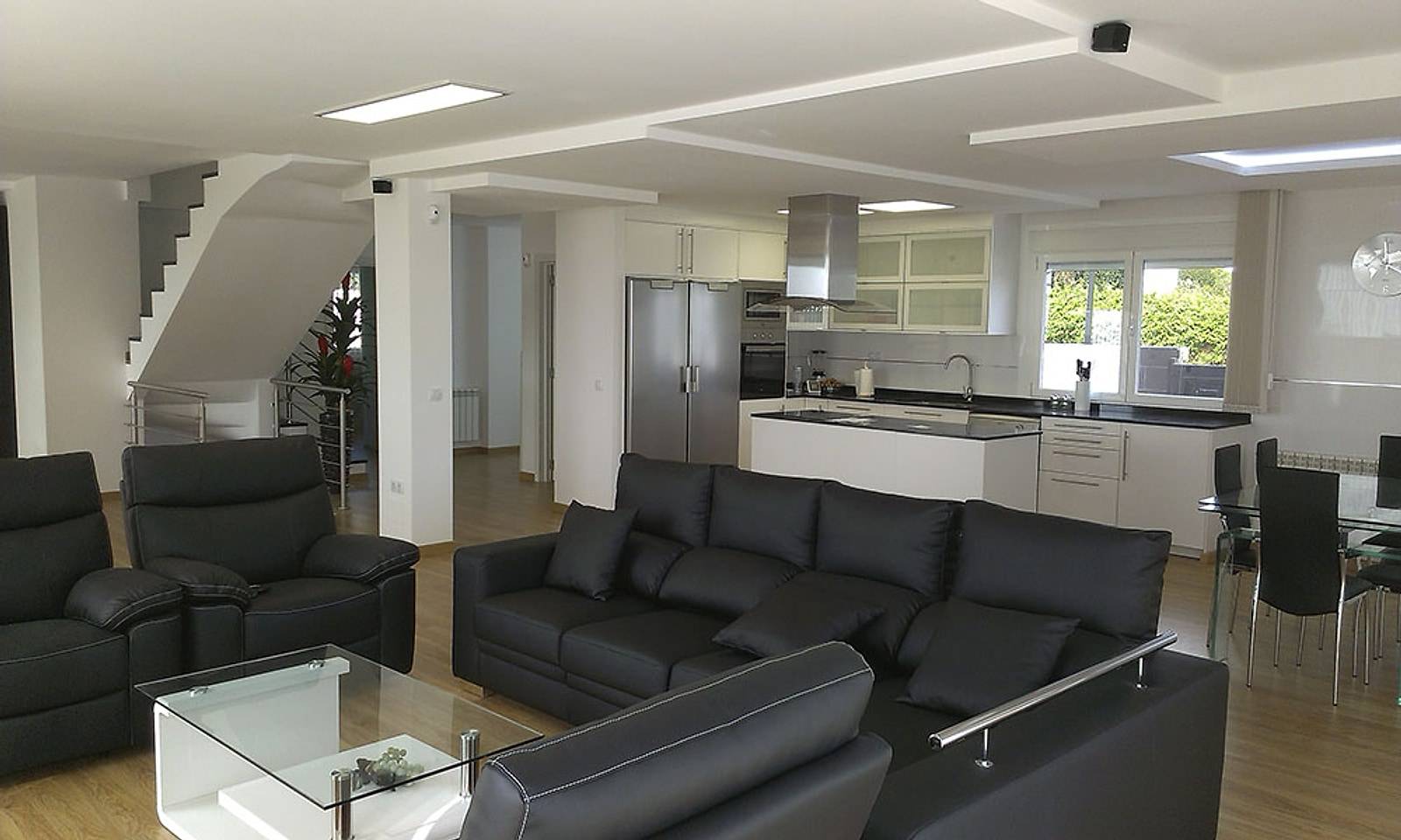 Planta baja del chalet abierta, con salón, cocina blanca con isla y la escalera al fondo