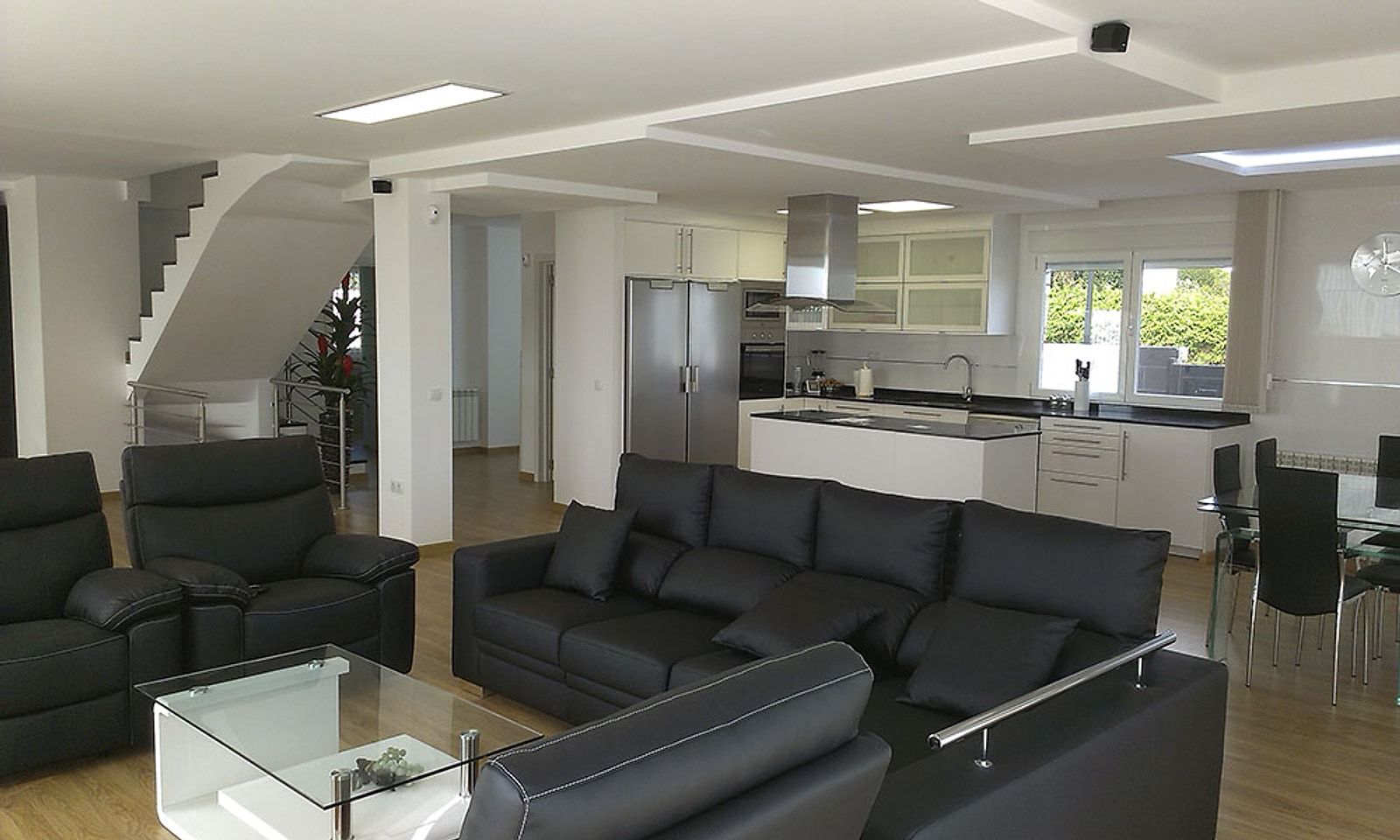 Planta baja del chalet abierta, con salón, cocina blanca con isla y la escalera al fondo