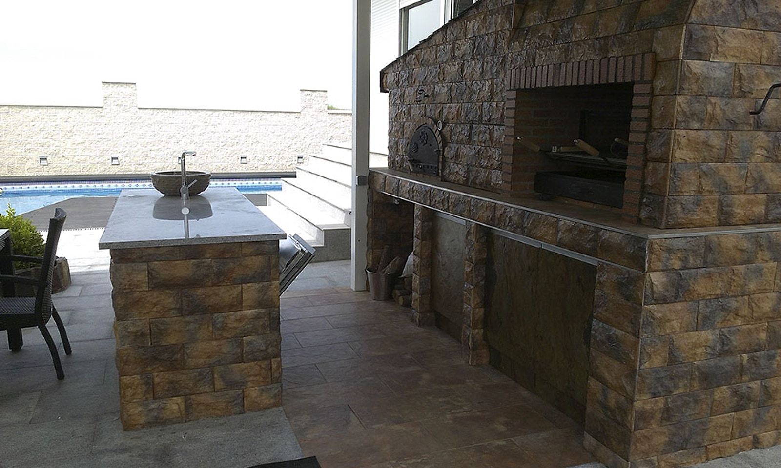 Horno y barbacoa de obra revestidos de piedra, junto a una isla con fregadero