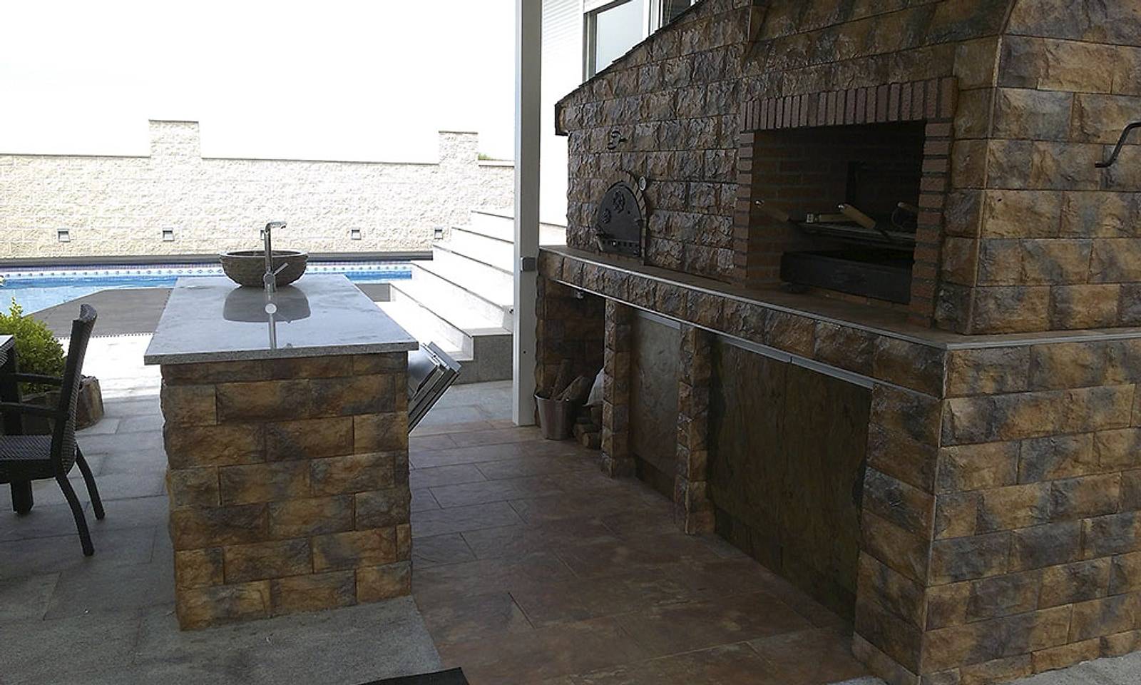 Horno y barbacoa de obra revestidos de piedra, junto a una isla con fregadero