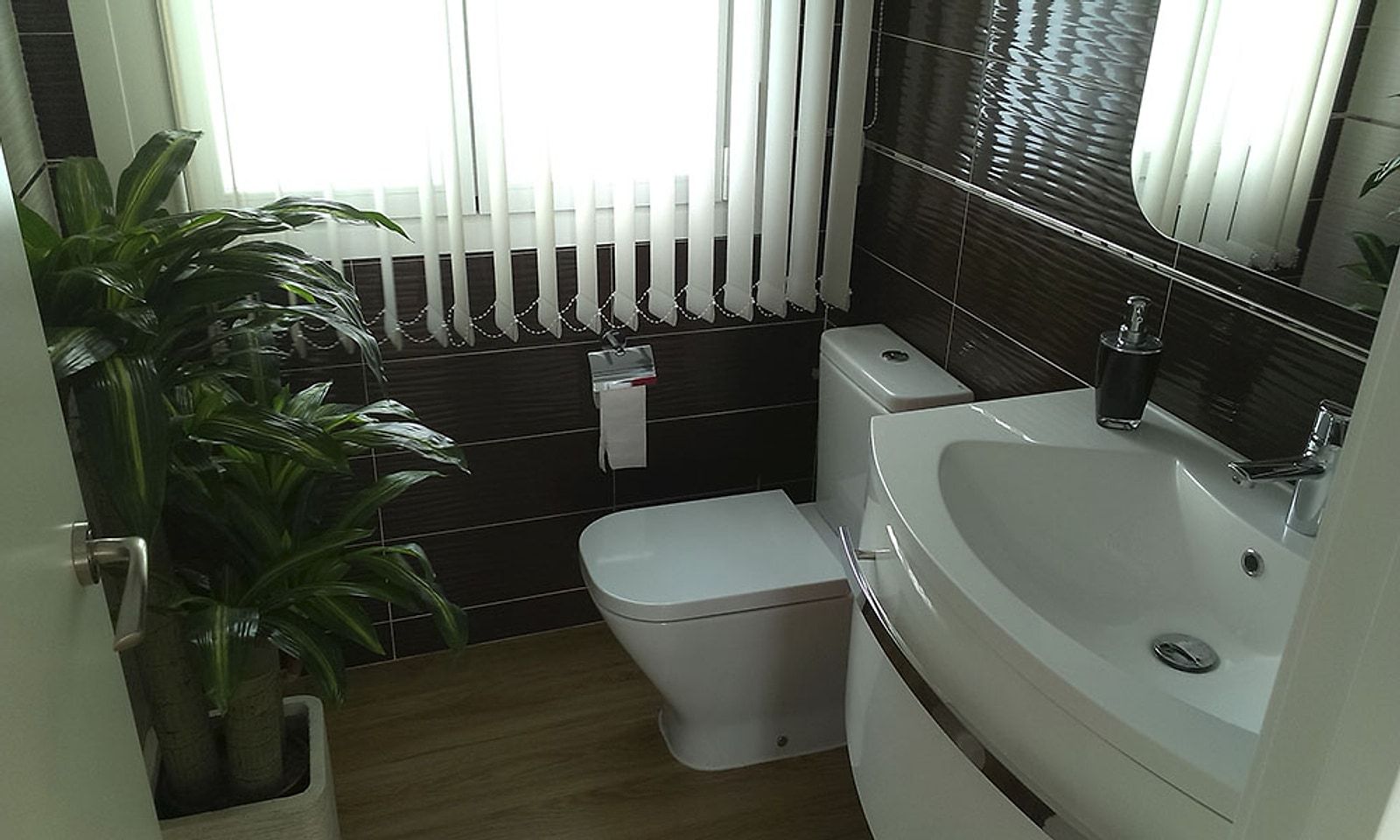 Baño del chalet con azulejo oscuro, lavabo blanco e inodoro