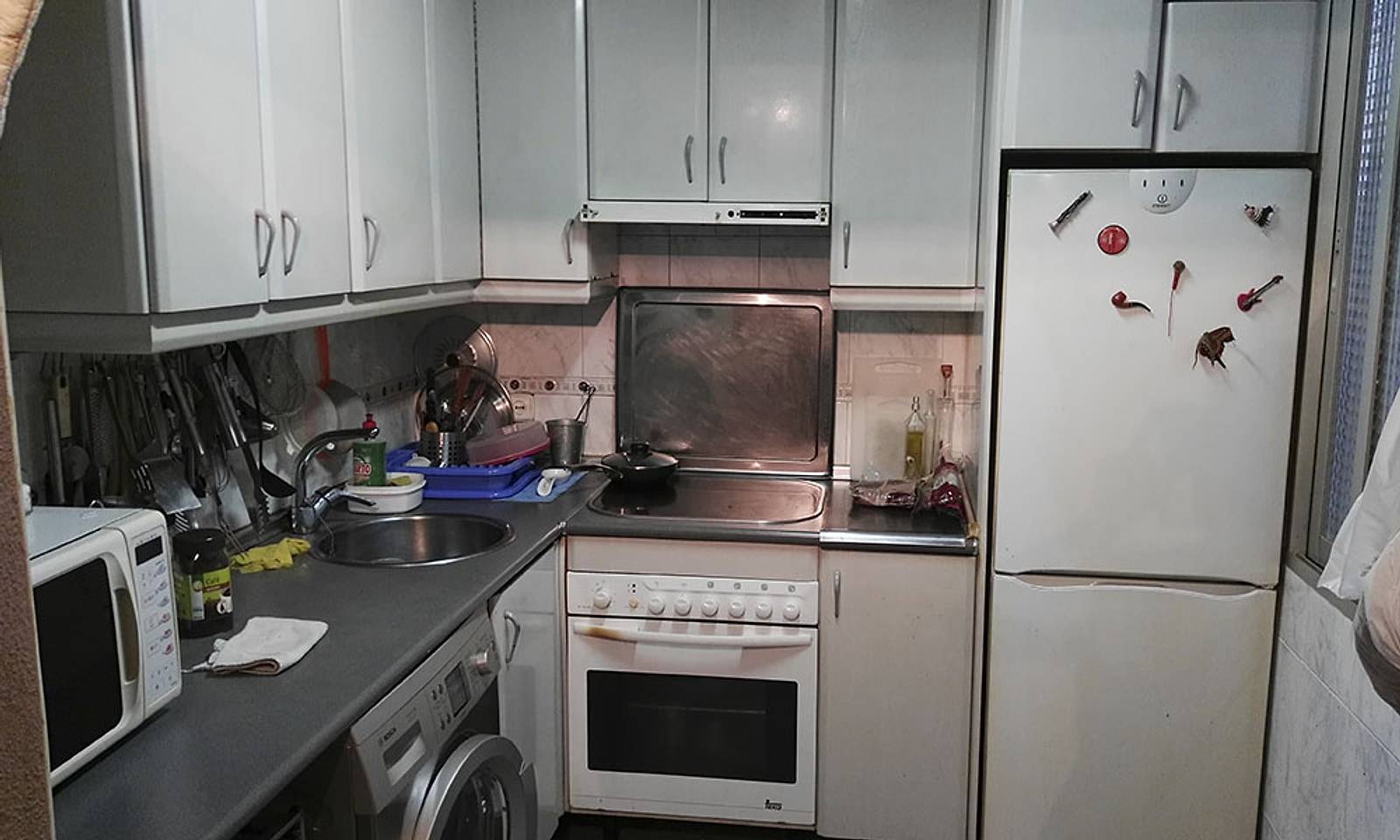 Cocina antigua de un piso, con muebles gastados y la encimera llena