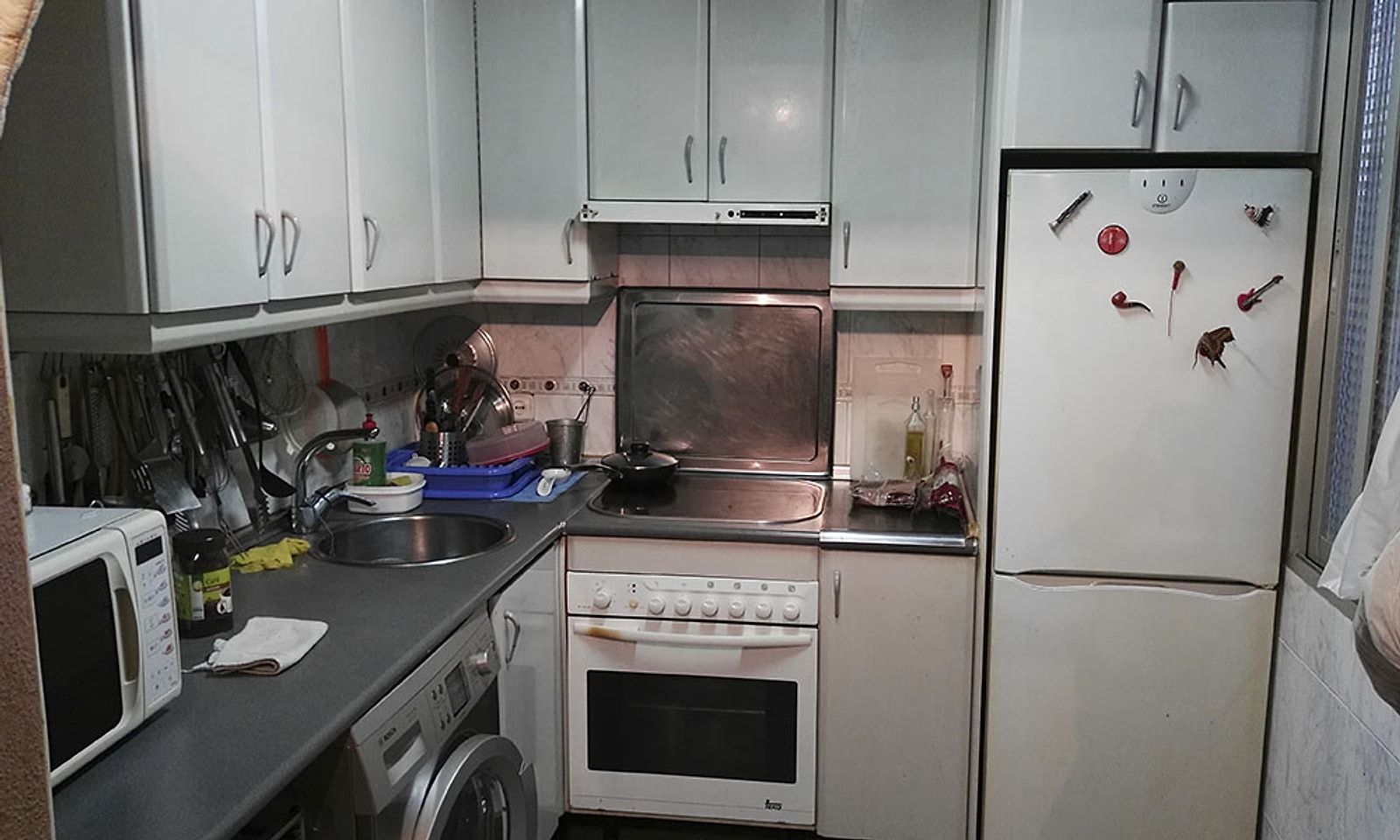 Cocina antigua de un piso, con muebles gastados y la encimera llena
