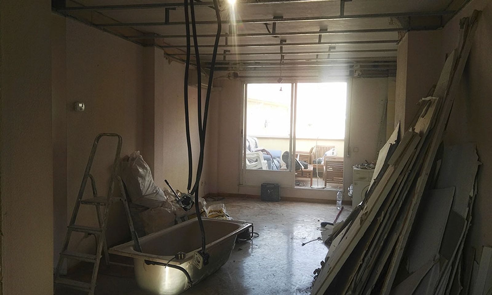 Salón de un piso en obra, con el techo abierto, escaleras de pintor y material apilado