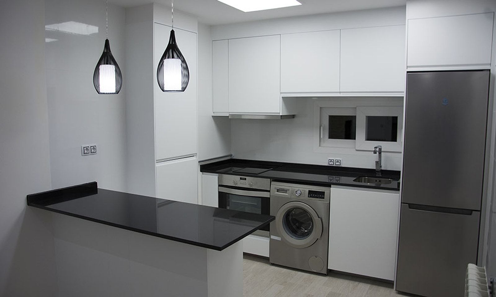 Cocina del piso reformada, con muebles blancos, barra negra y lámparas colgantes