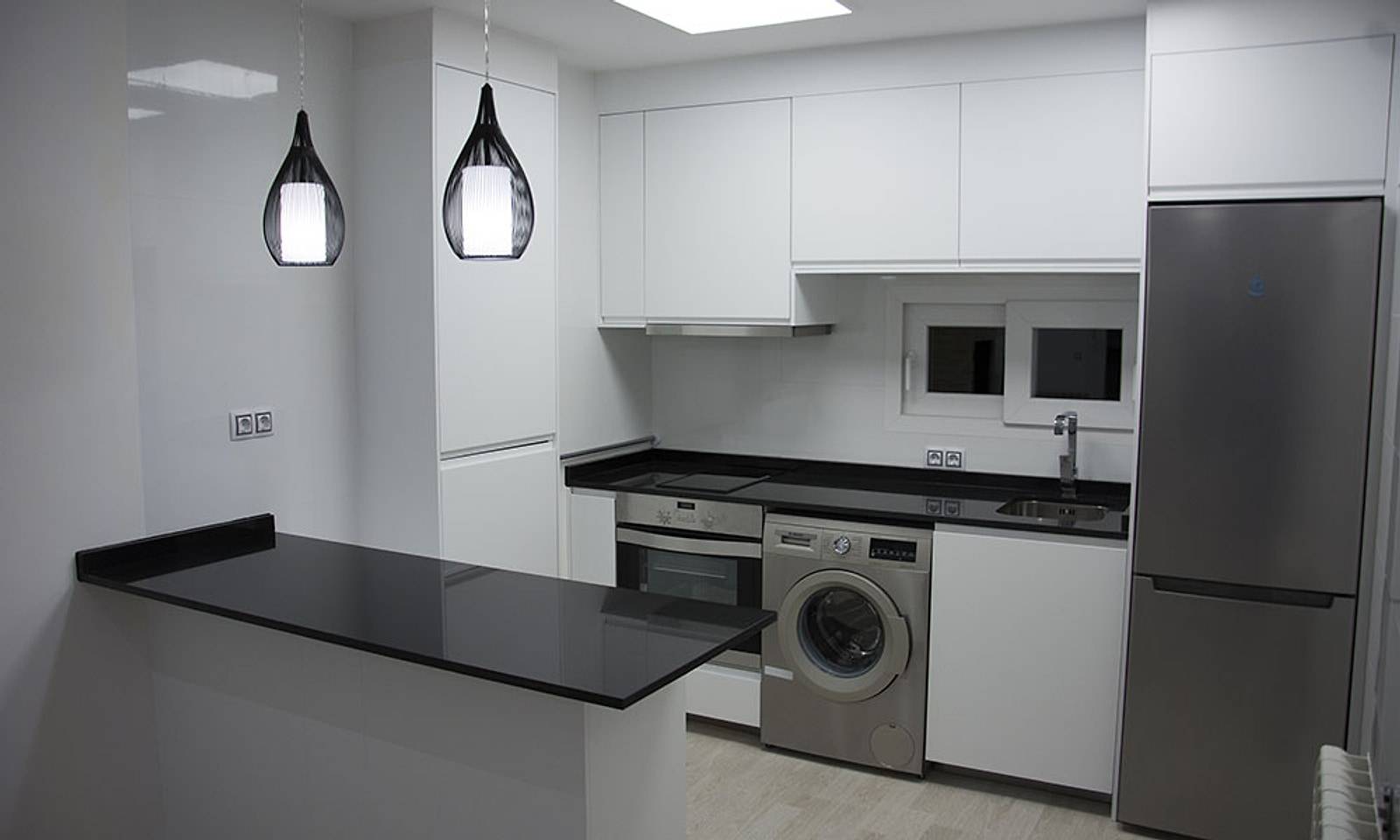 Cocina del piso reformada, con muebles blancos, barra negra y lámparas colgantes