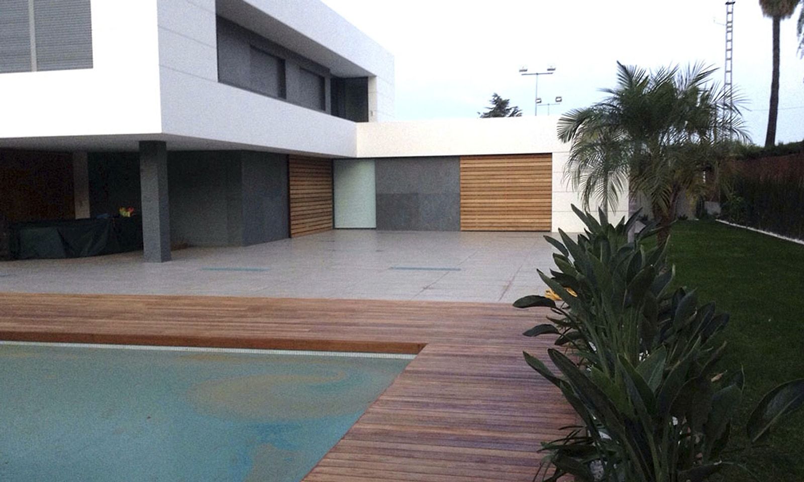 Piscina rodeada de tarima de madera tropical, con el chalet y el porche al fondo