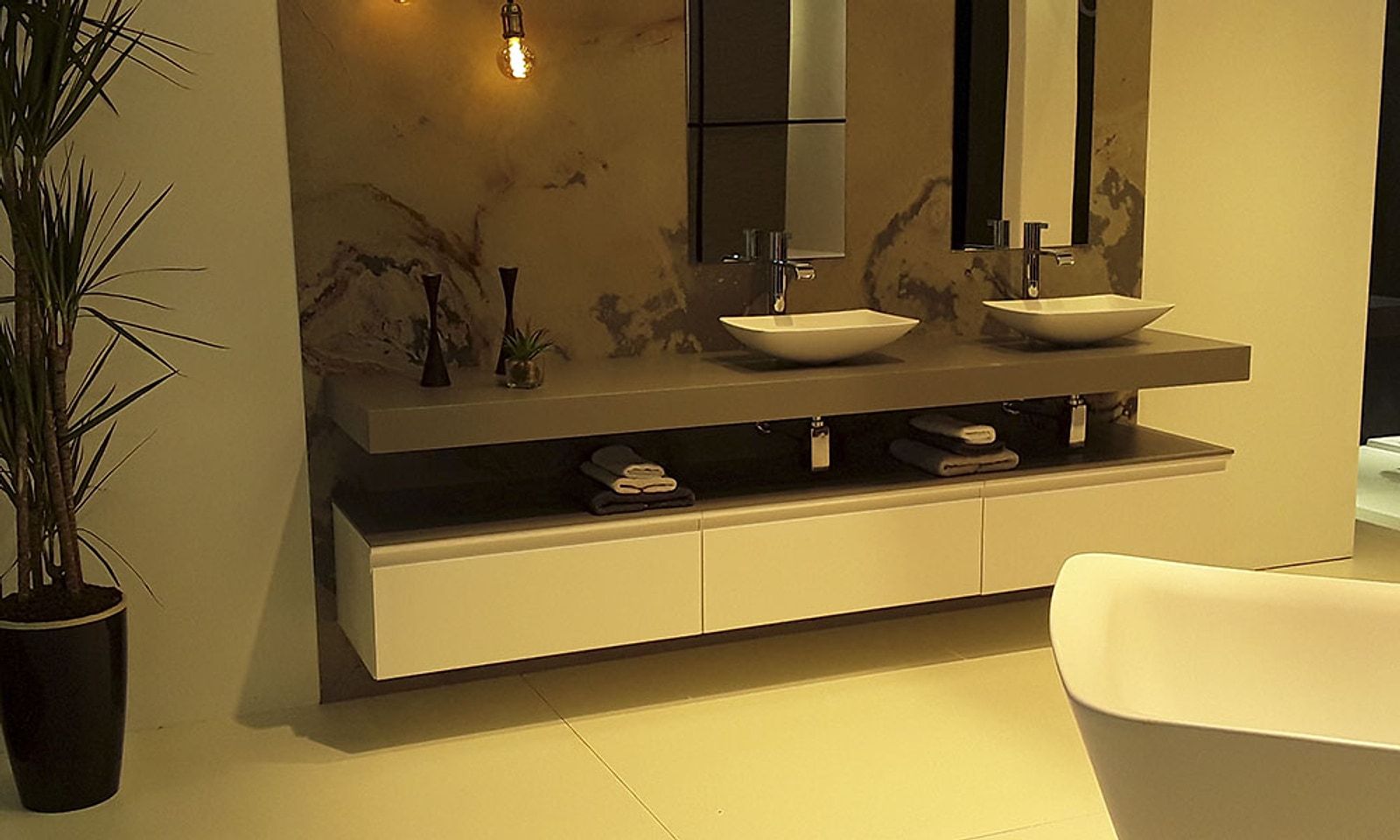 Baño con dos lavabos sobre encimera, grifería de caño alto y una bañera exenta en primer plano