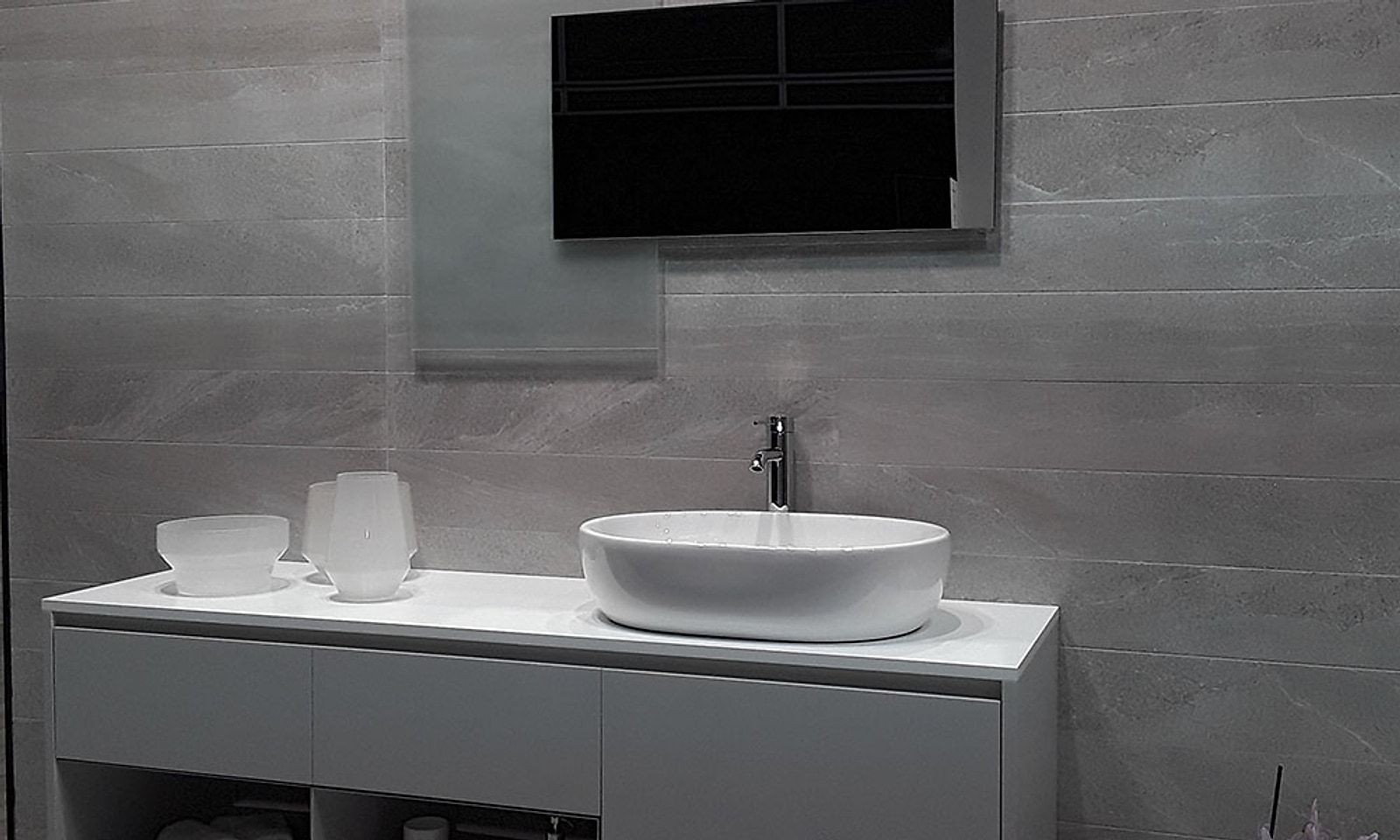 Lavabo sobre encimera blanca con porcelánico gris de gran formato en la pared