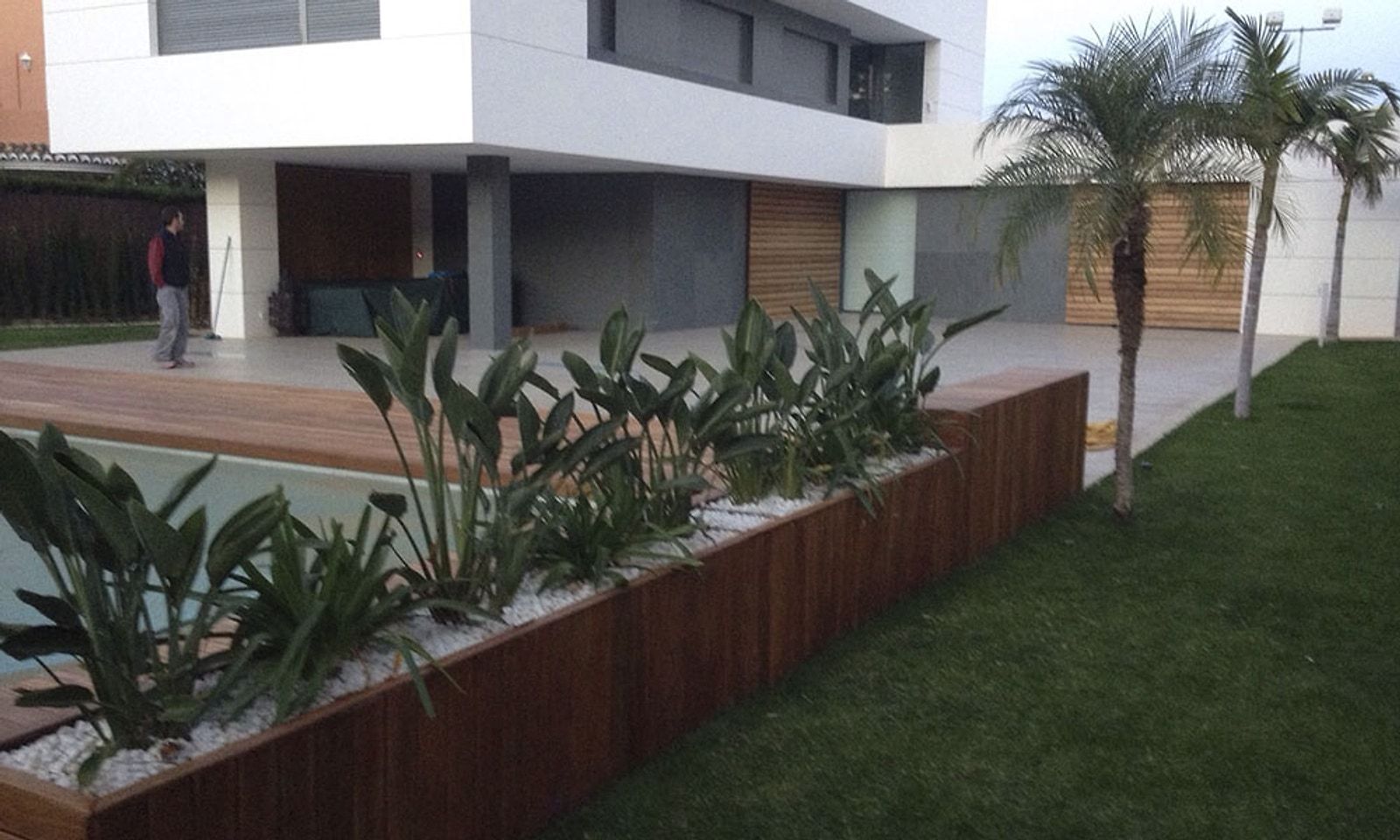 Jardinera forrada de madera con plantas junto a la piscina y el césped