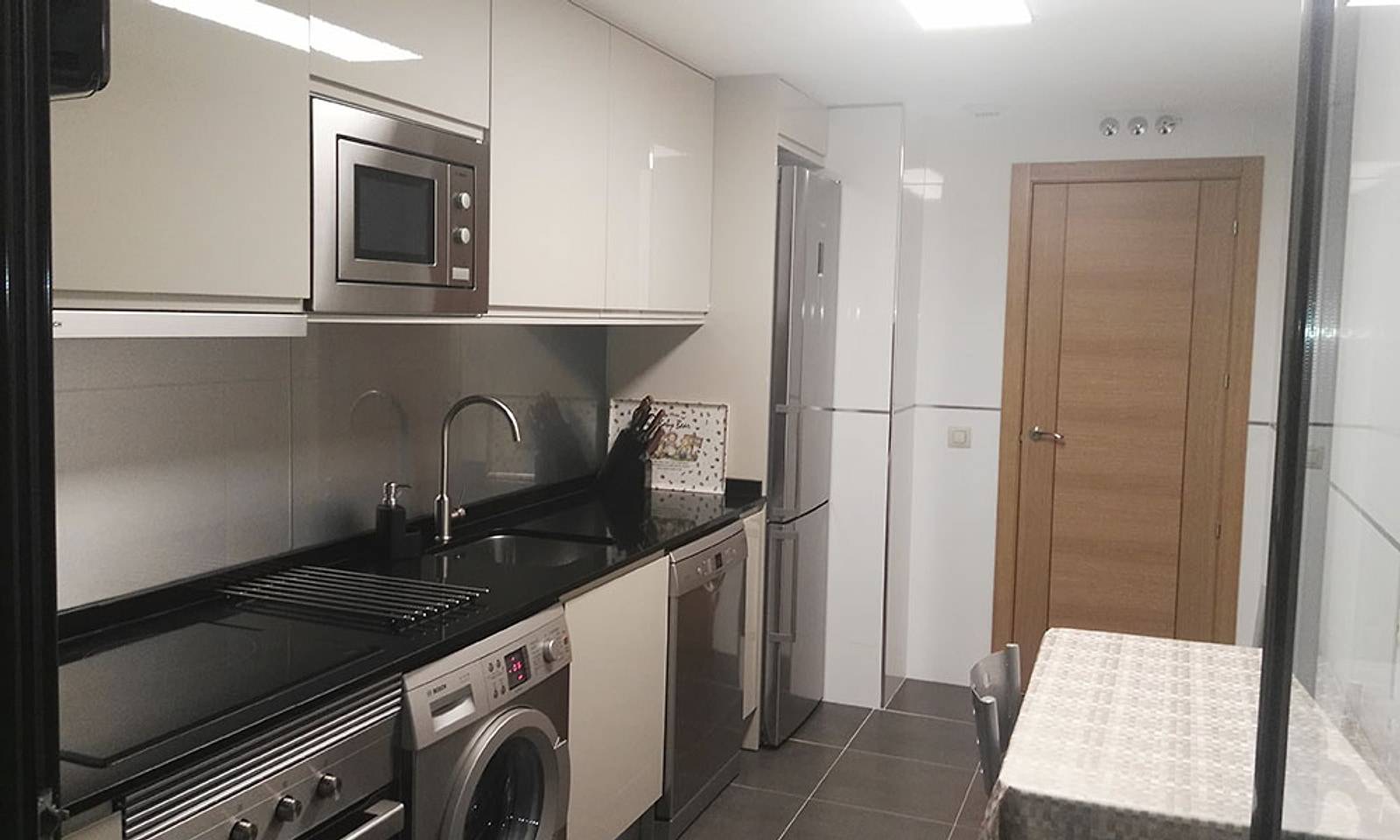 La misma cocina terminada, con muebles blancos, encimera negra y electrodomésticos de acero
