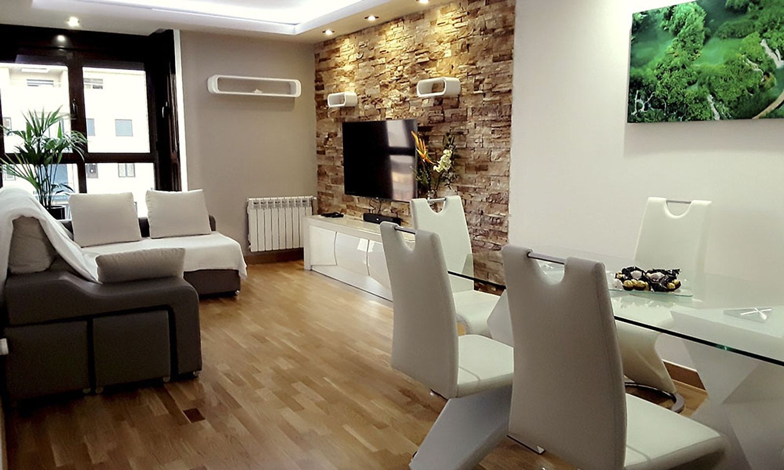 Salón del piso reformado, con pared de piedra iluminada, sofá y mesa de comedor