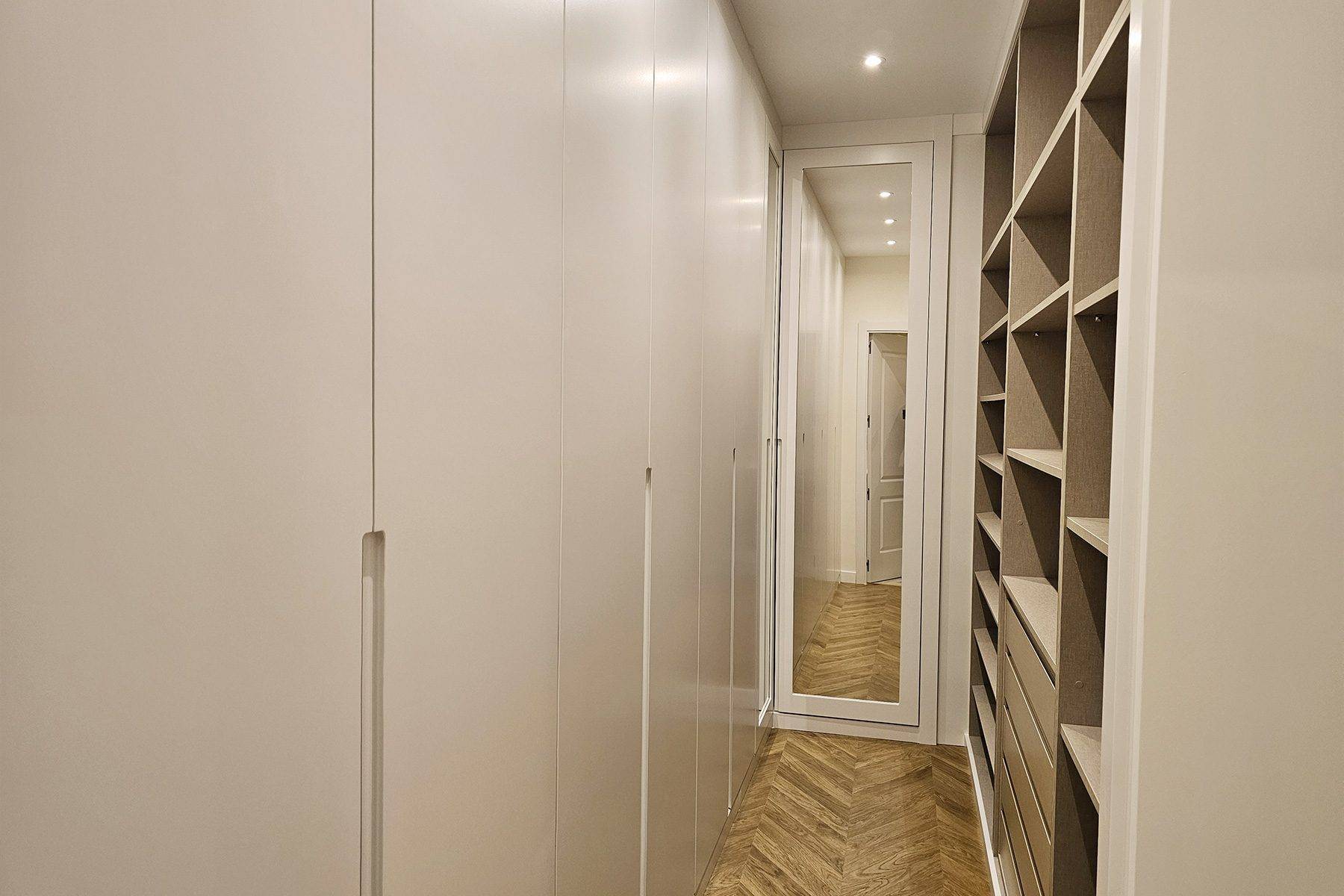 Vestidor con armarios blancos hasta el techo, baldas abiertas y una puerta con espejo